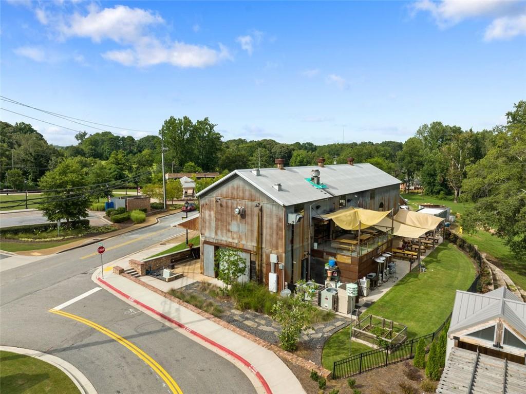 Aerial view of rustic two-story barn with metal roof, shaded outdoor patio, umbrellas, trees, and roads in Wehunt Meadows, Hoschton, Georgia