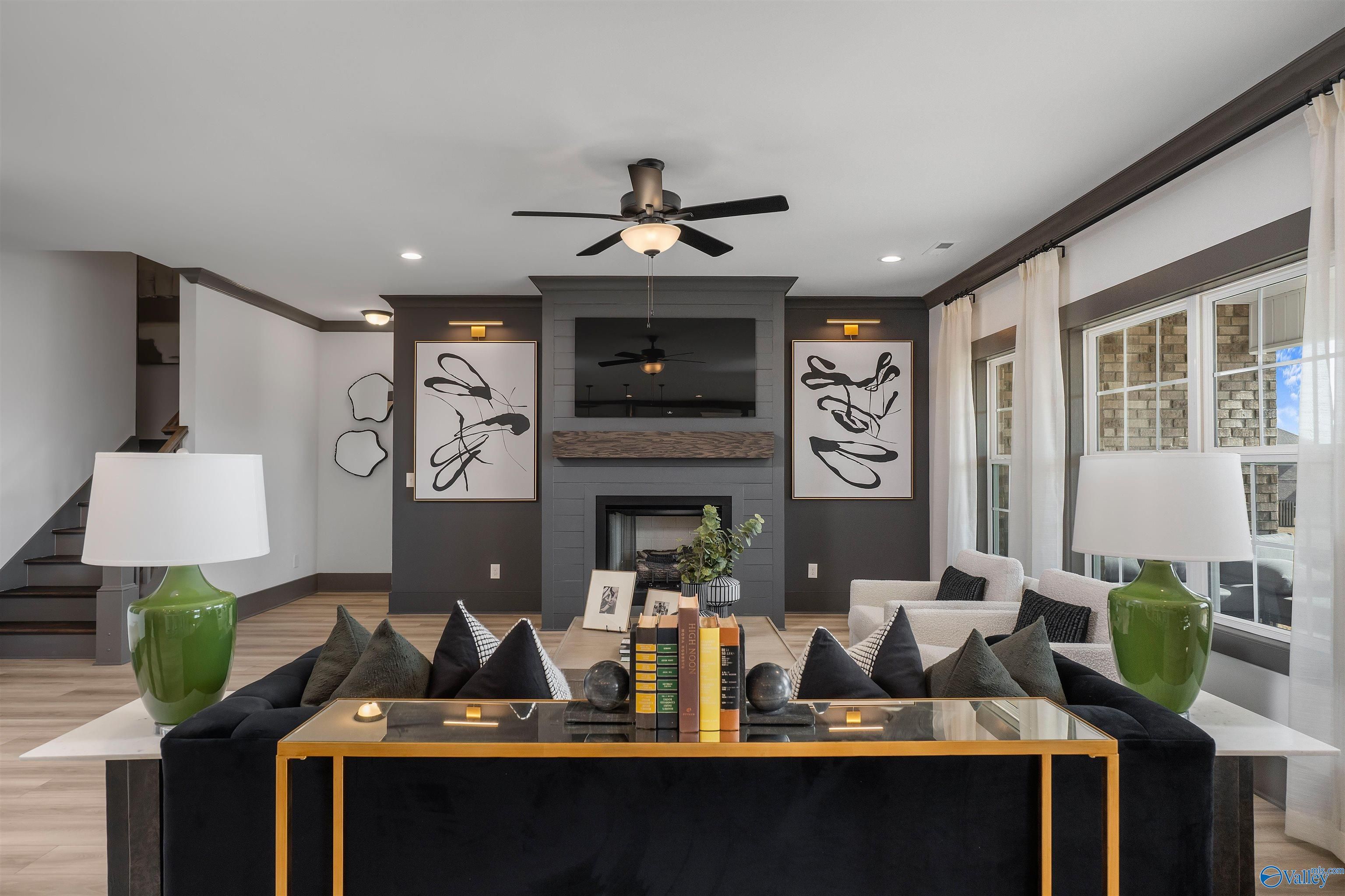 Cozy living room featuring modern fireplace, black velvet sectional sofa, abstract art, and ceiling fans in Davidson Homes The Rockford B, Madison, Alabama