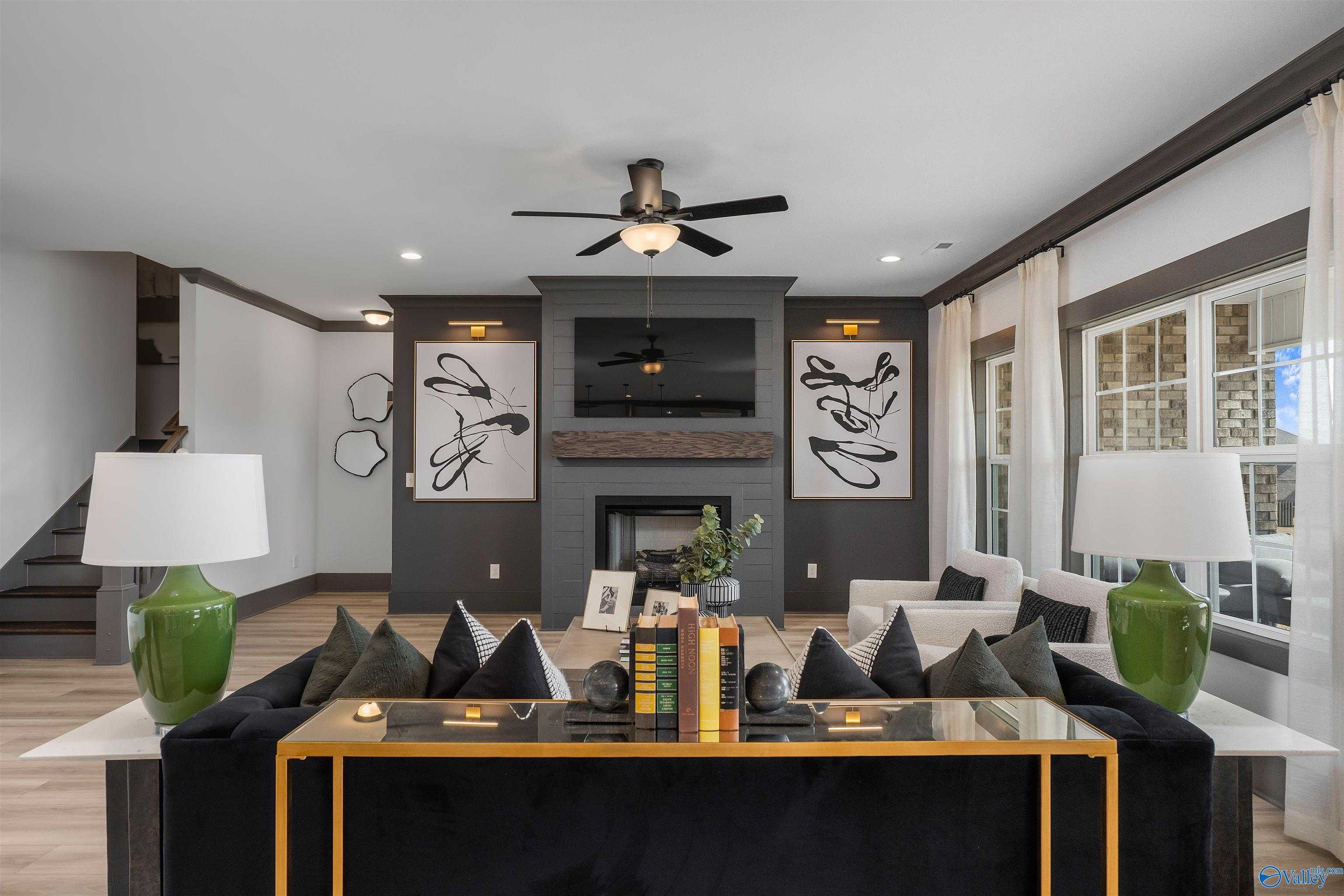Cozy living room featuring modern fireplace, black velvet sectional sofa, abstract art, and ceiling fans in Davidson Homes The Rockford B, Madison, Alabama