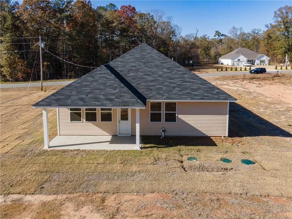 Aerial view of The Orion 4-bedroom single-story home rear with covered porch, tan siding, dark roof amid autumn woods in Silver Oak, Cusseta, Alabama