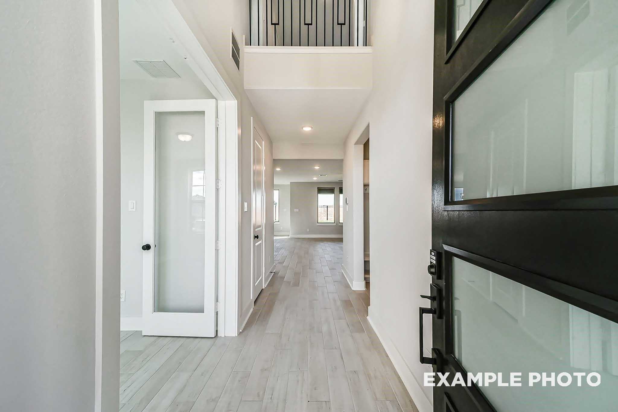 Elegant entry hallway with light oak floors, frosted glass doors, and modern black frame in Davidson Homes The Philip C, Rosharon, Texas