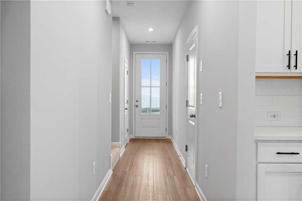 Bright hallway with light gray walls, oak hardwood floors, white doors, and kitchen cabinets in The Durant A, Emerson, Georgia