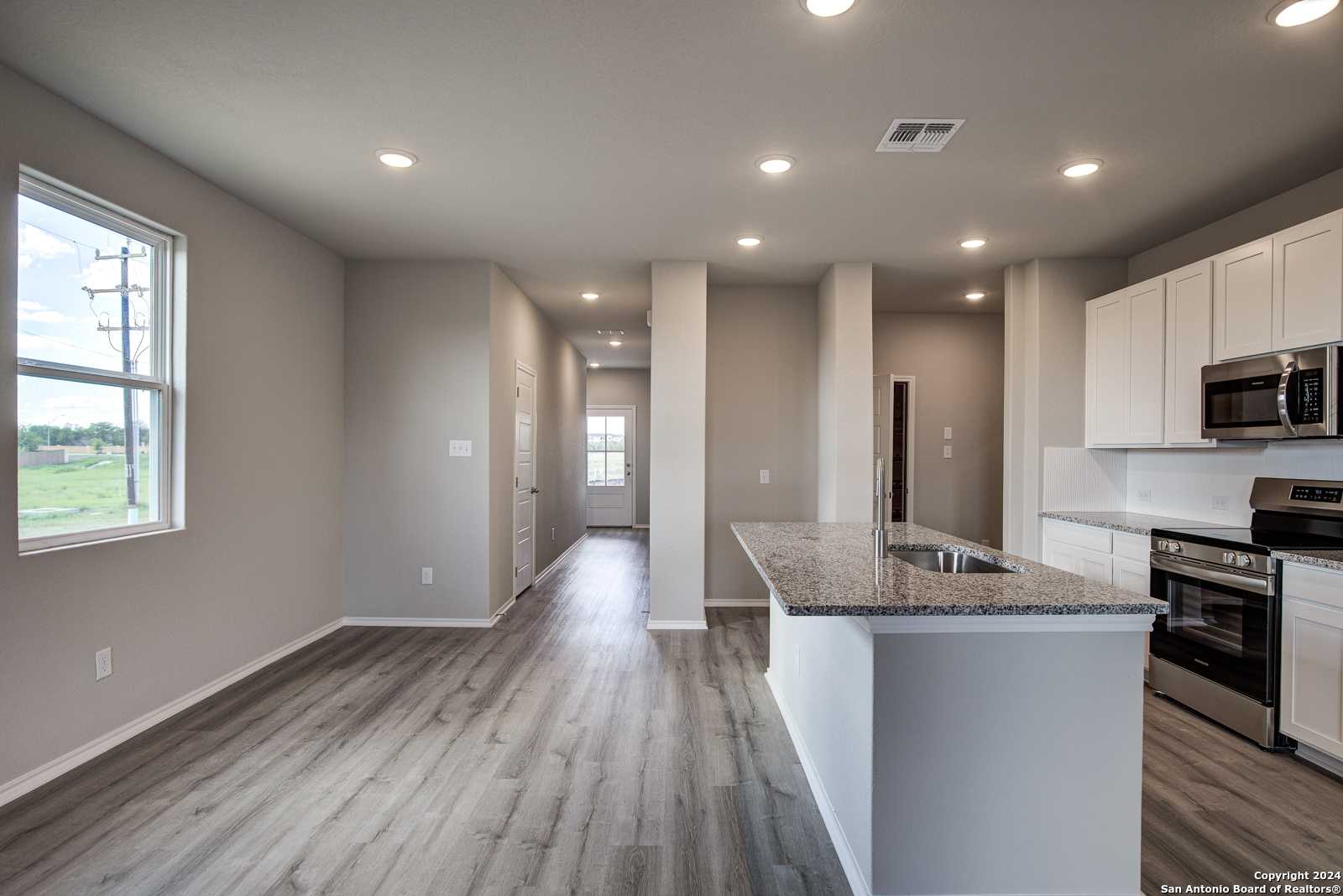 Open-concept kitchen and living area with granite island, stainless appliances, hardwood floors in The Blanco C, Davidson Homes, San Antonio