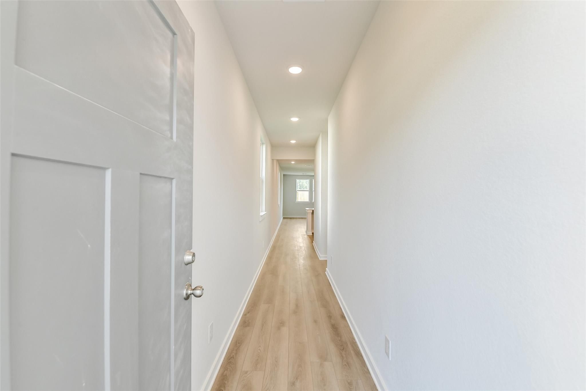 Bright hallway with light oak floors, white walls, and recessed lights in Davidson Homes The Colorado F, Cleveland, Texas