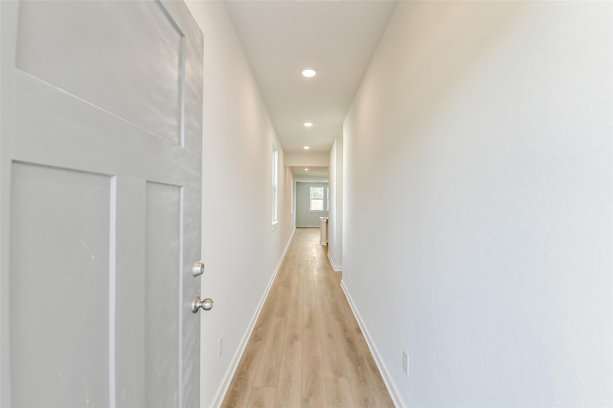 Bright hallway with open white door, recessed lights, and light oak floors in Davidson Homes The Colorado F, Cleveland, Texas