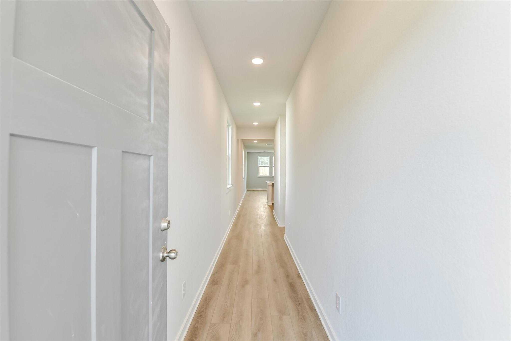 Bright hallway with light oak floors, white walls, and recessed lights in Davidson Homes The Colorado F, Cleveland, Texas