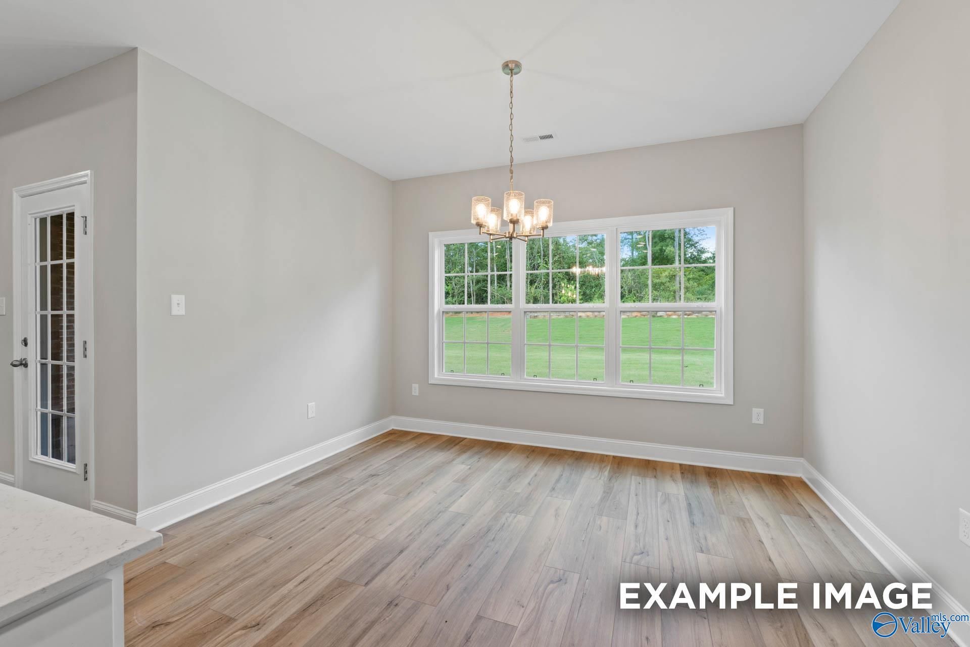 Sunlit dining room with hardwood floors, chandelier, and large windows overlooking green lawn in Davidson Homes The Montgomery, Meridianville