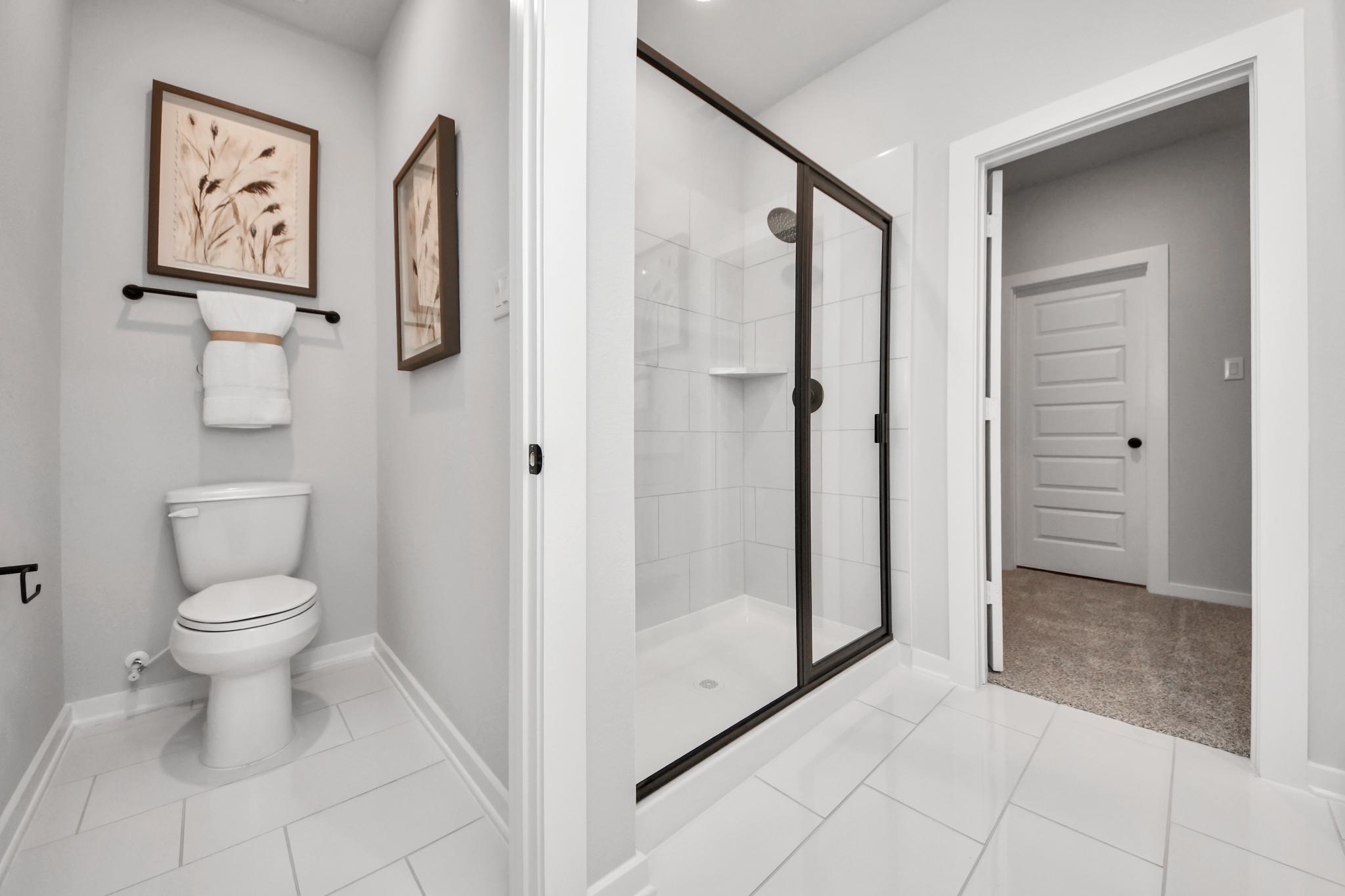 Modern bathroom at Robins Landing in Houston with walk-in glass shower, white tile flooring, and sleek finishes by Davidson.