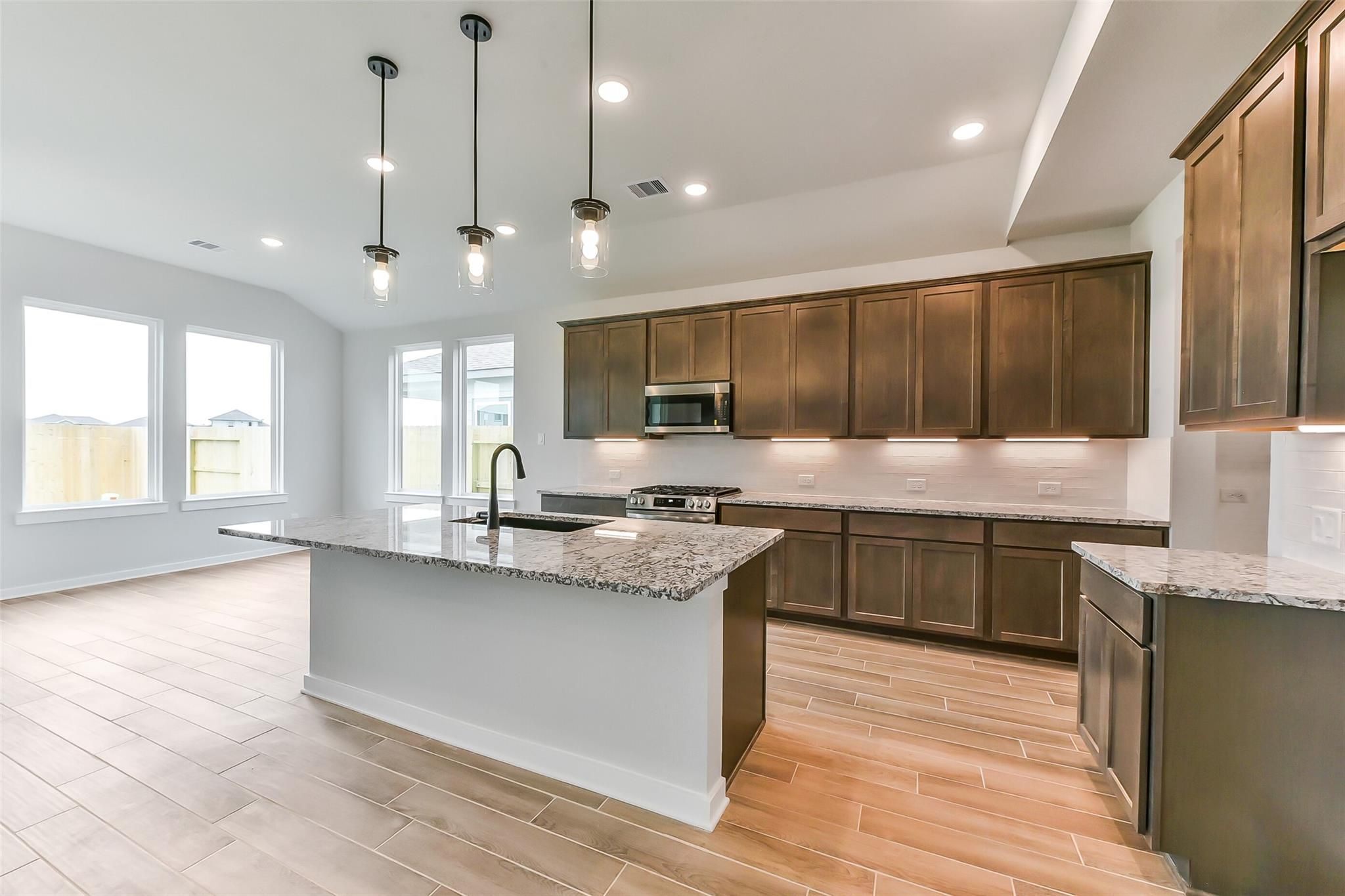 Modern kitchen with granite island, shaker cabinets, stainless appliances, pendant lights in Davidson Homes Sequoia C, Crosby TX