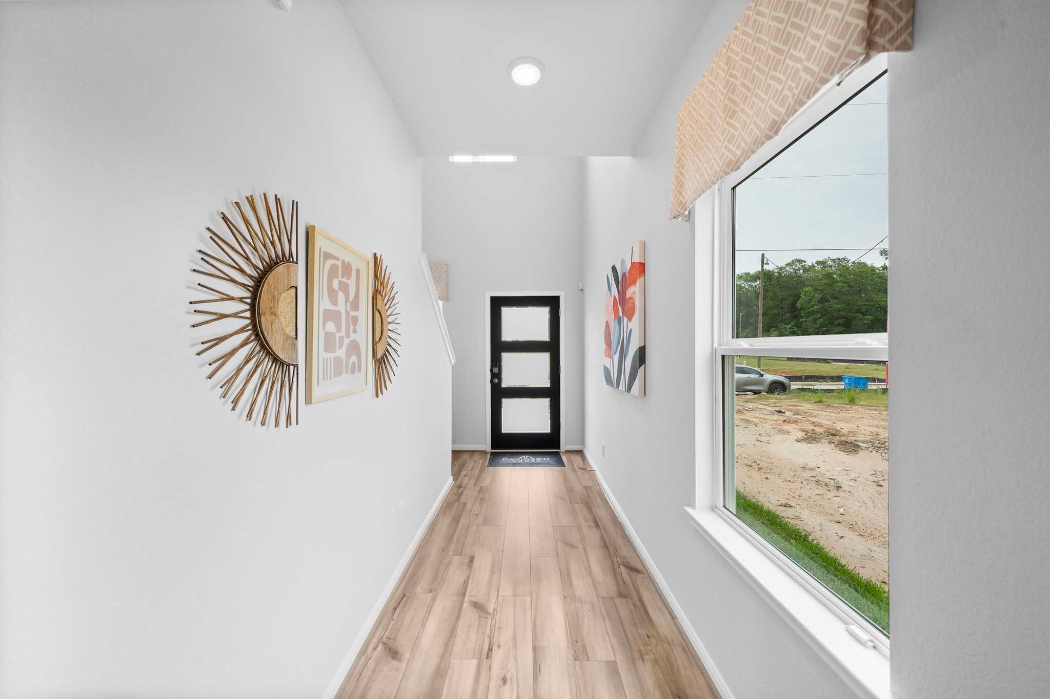 Spacious hallway interior at Hill & Dale Ranch in Splendora Texas with light wood floors white walls framed art and window view