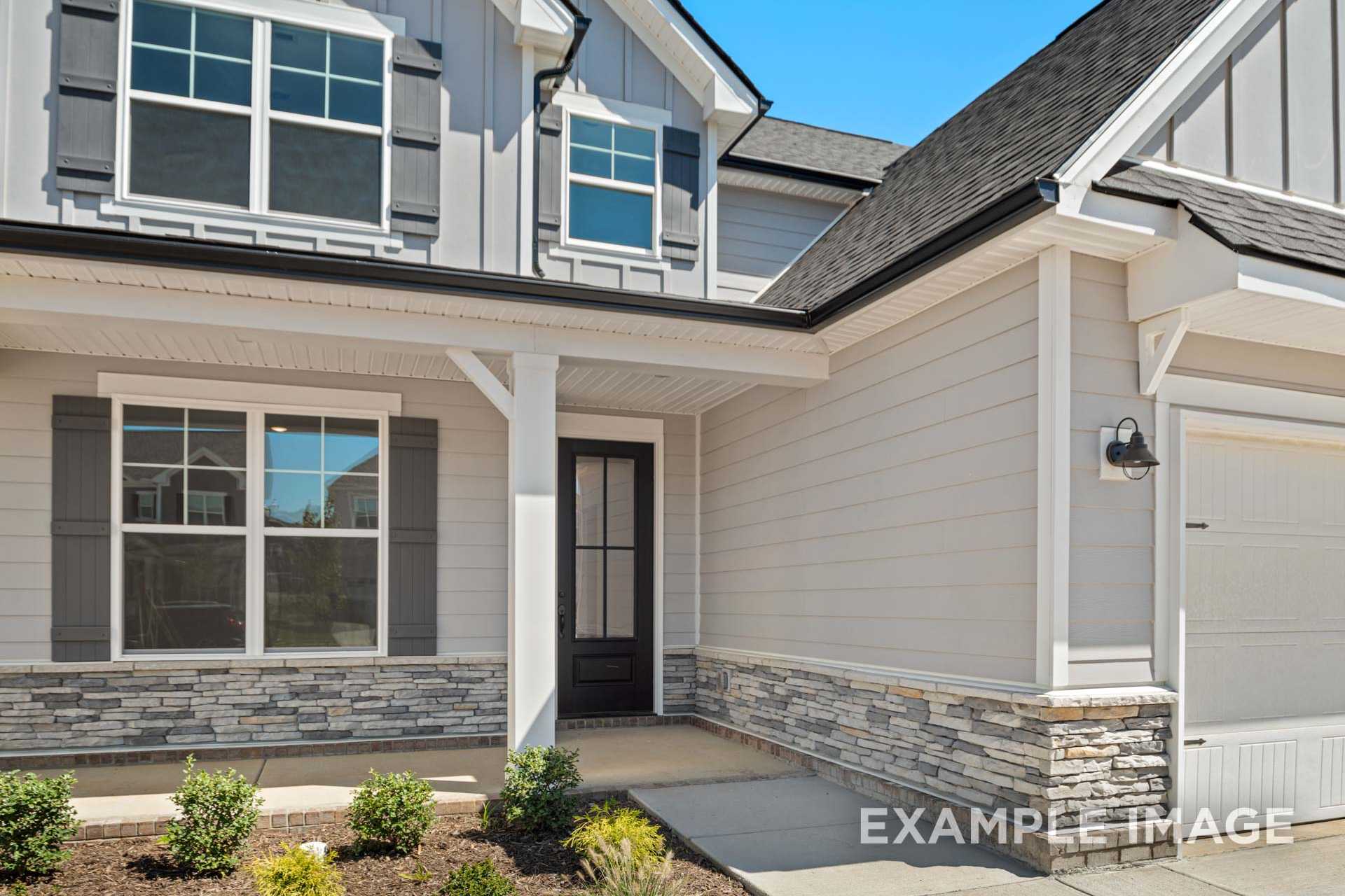 Modern two-story The Ash B home elevation featuring gray siding, stone accents, covered porch, and two-car garage
