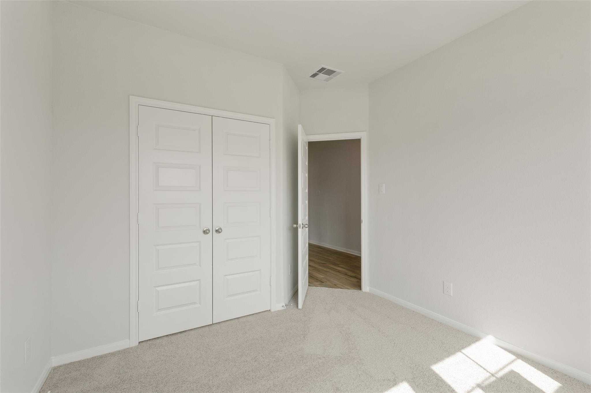 Bright secondary bedroom with double white closet doors and open doorway in Davidson Homes The Laguna B, Dayton, Texas