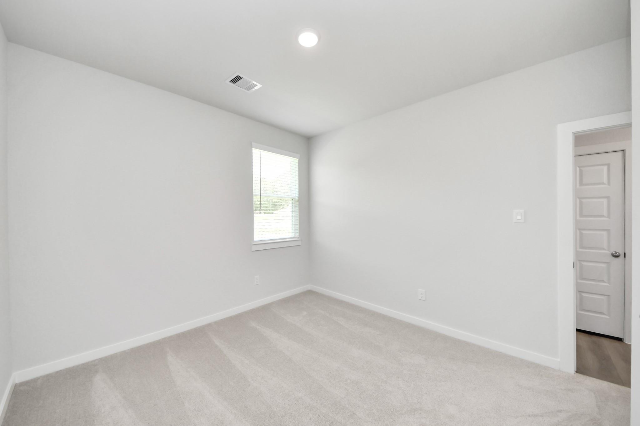 Bright, carpeted bedroom with neutral walls in The Frio F floor plan at Liberty Estates, Cleveland, Texas.