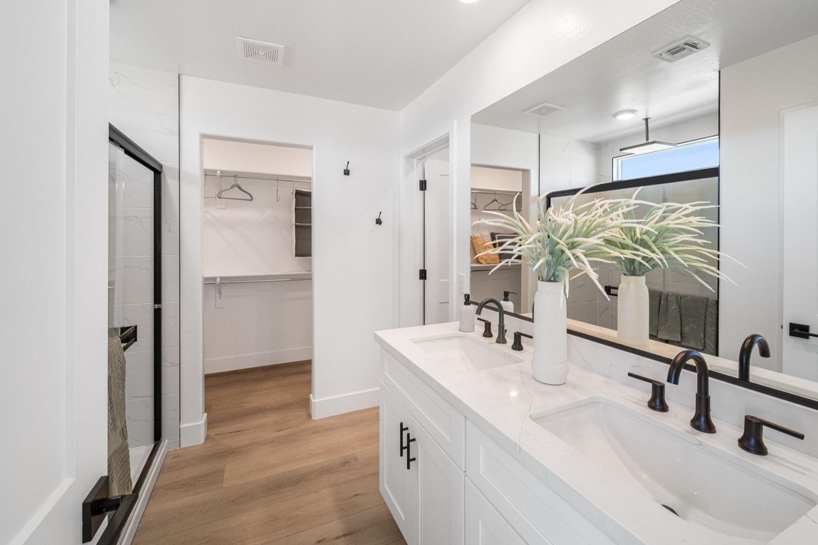 Modern master bathroom in The Wilmington A with white double vanity, glass walk-in shower, and adjacent closet on hardwood floors