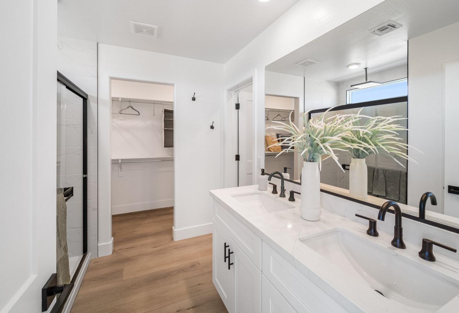 Modern master bathroom in The Wilmington A with white double vanity, glass walk-in shower, and adjacent closet on hardwood floors