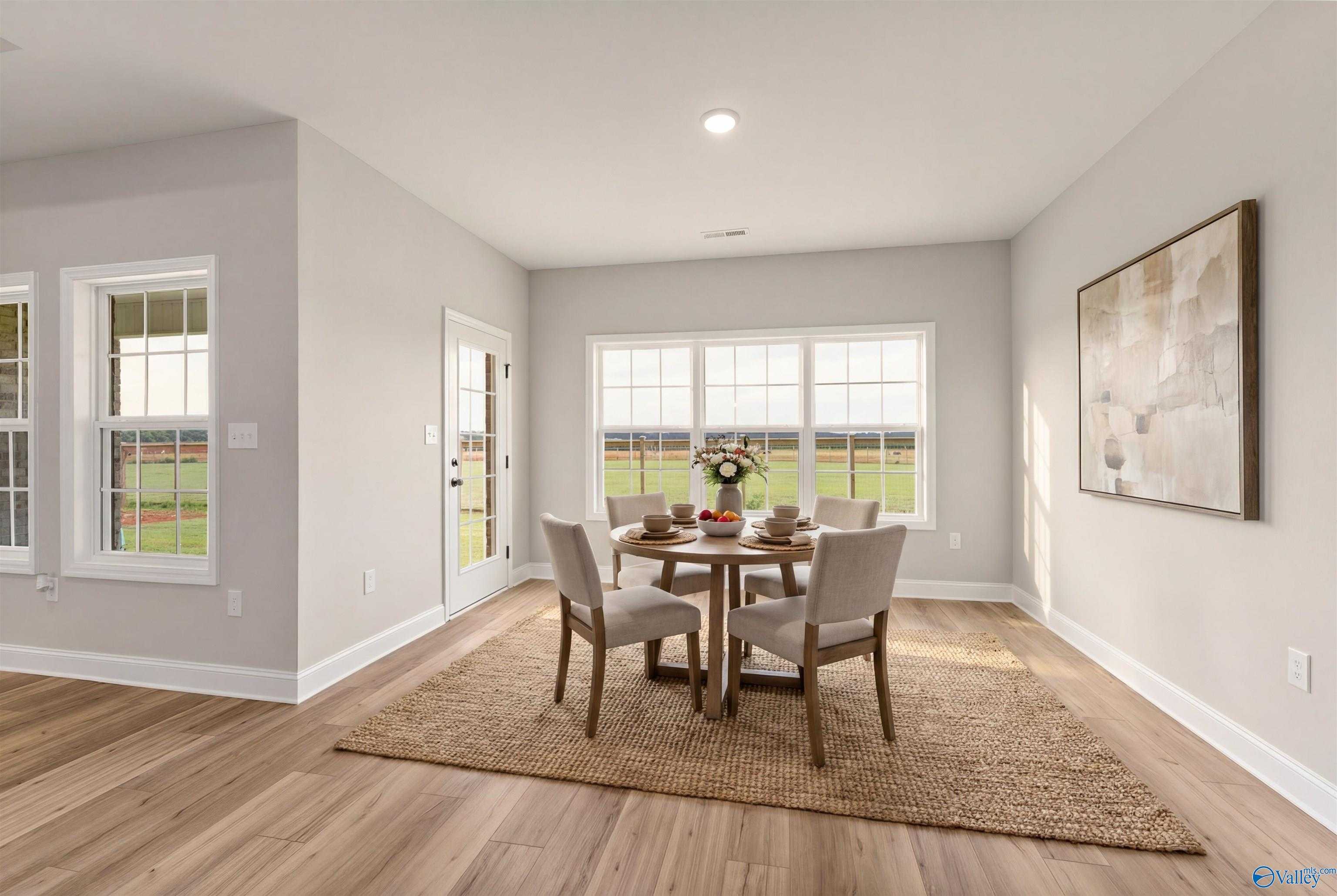 Bright dining room with round wooden table, upholstered chairs, and large windows overlooking fields in The Finleigh home, Toney, Alabama