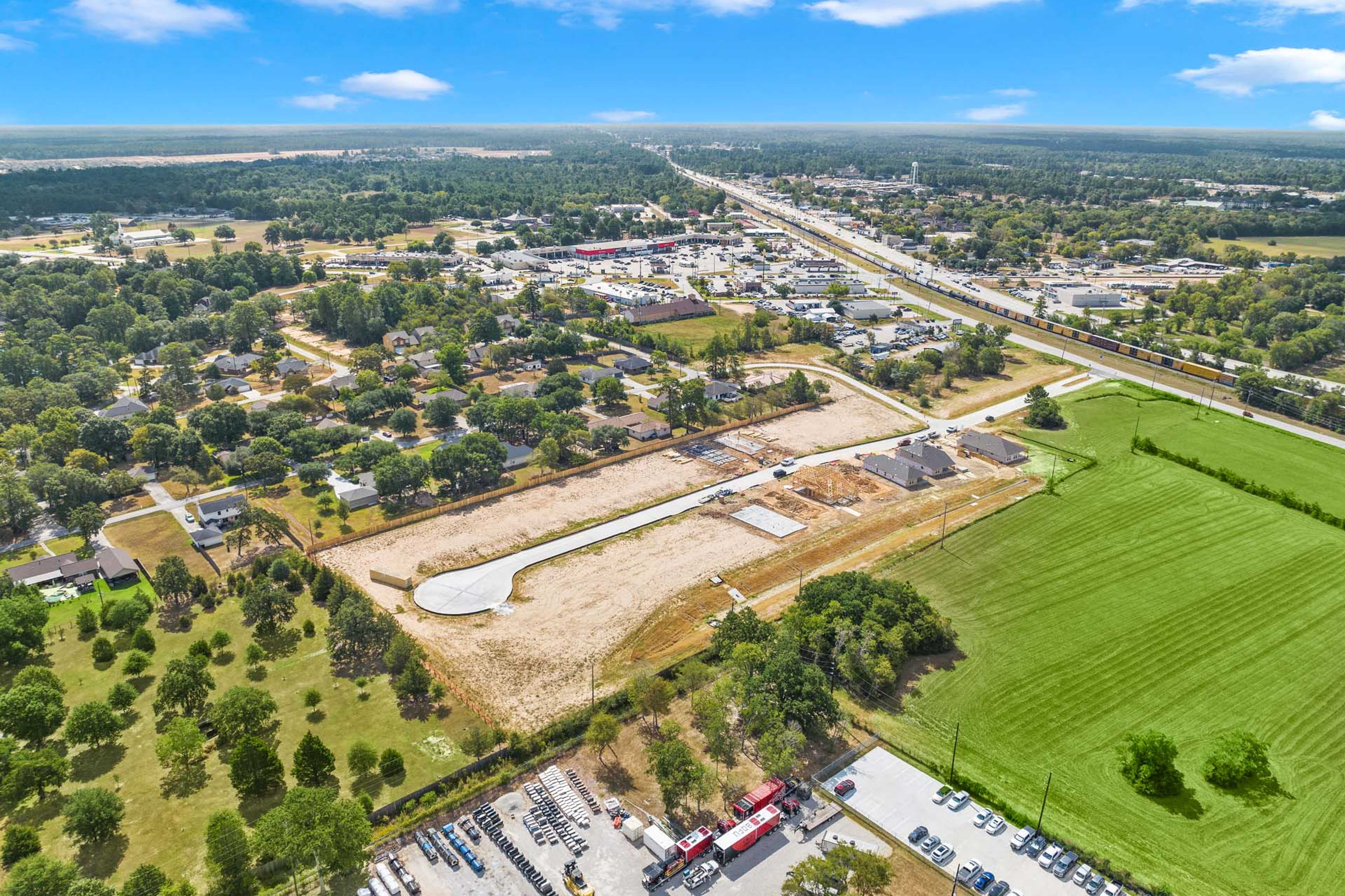 Aerial view of Windmill Estates development in Magnolia Texas with construction site, cleared lots, new structures, green fields, and surrounding trees