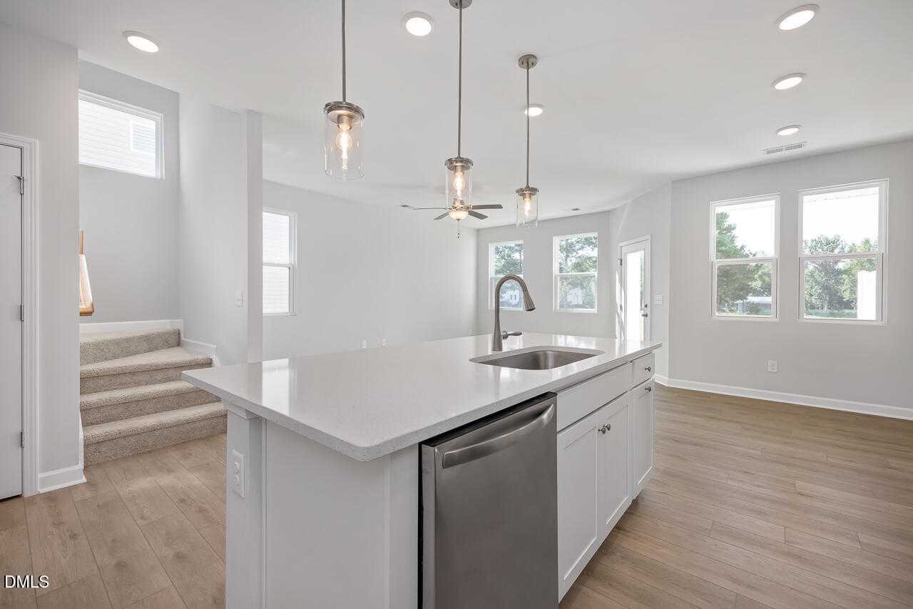 Bright open-concept kitchen with white quartz island, stainless sink, dishwasher, pendant lights in Davidson Homes The Graham, Fuquay-Varina, NC
