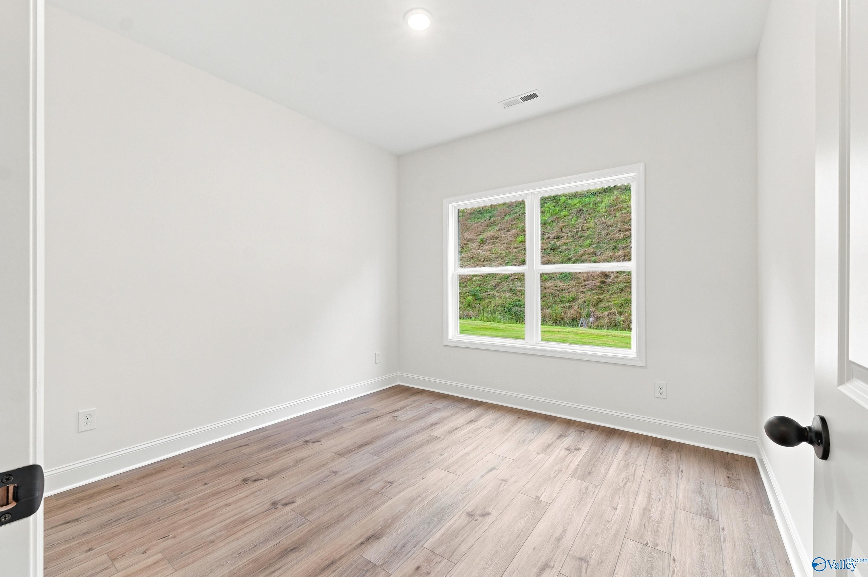 Bright bedroom with wood-look flooring and large window in The Shelby D floor plan at Noble Ridge, Cullman, Alabama.