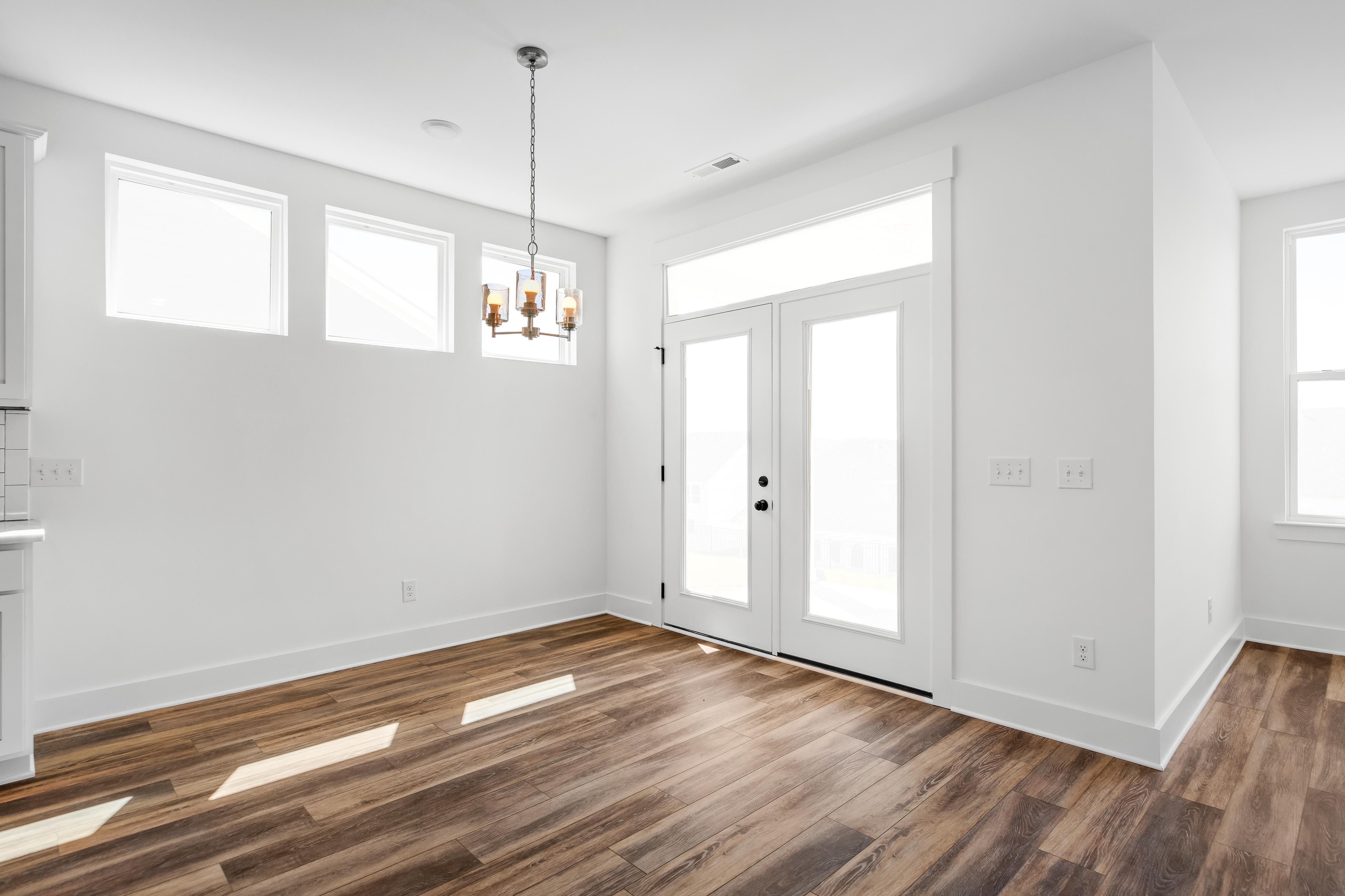 Bright dining area in The Cedar D featuring modern light fixture, wood-look flooring, and glass patio doors.