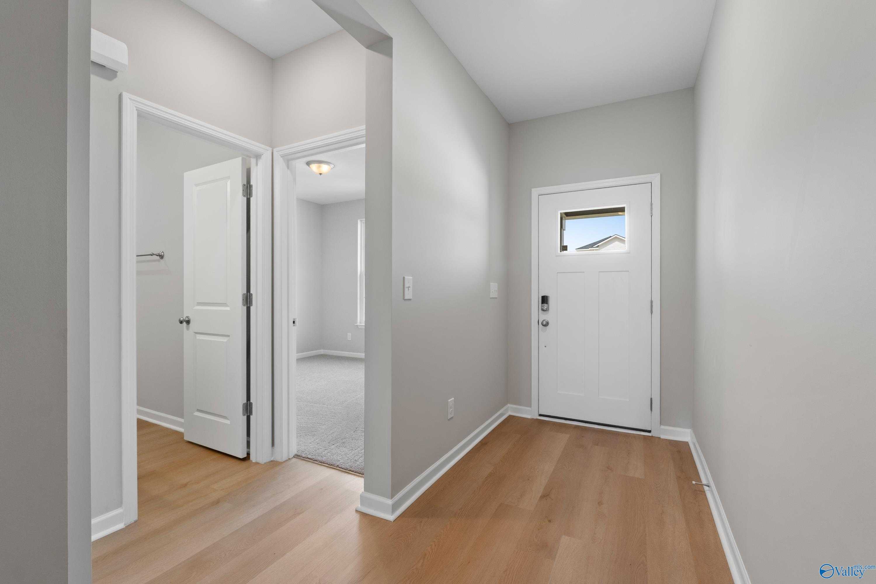 Bright entryway with hardwood floors, white front door and adjacent bedroom door in The Aurora 4-bedroom home, Harvest, Alabama