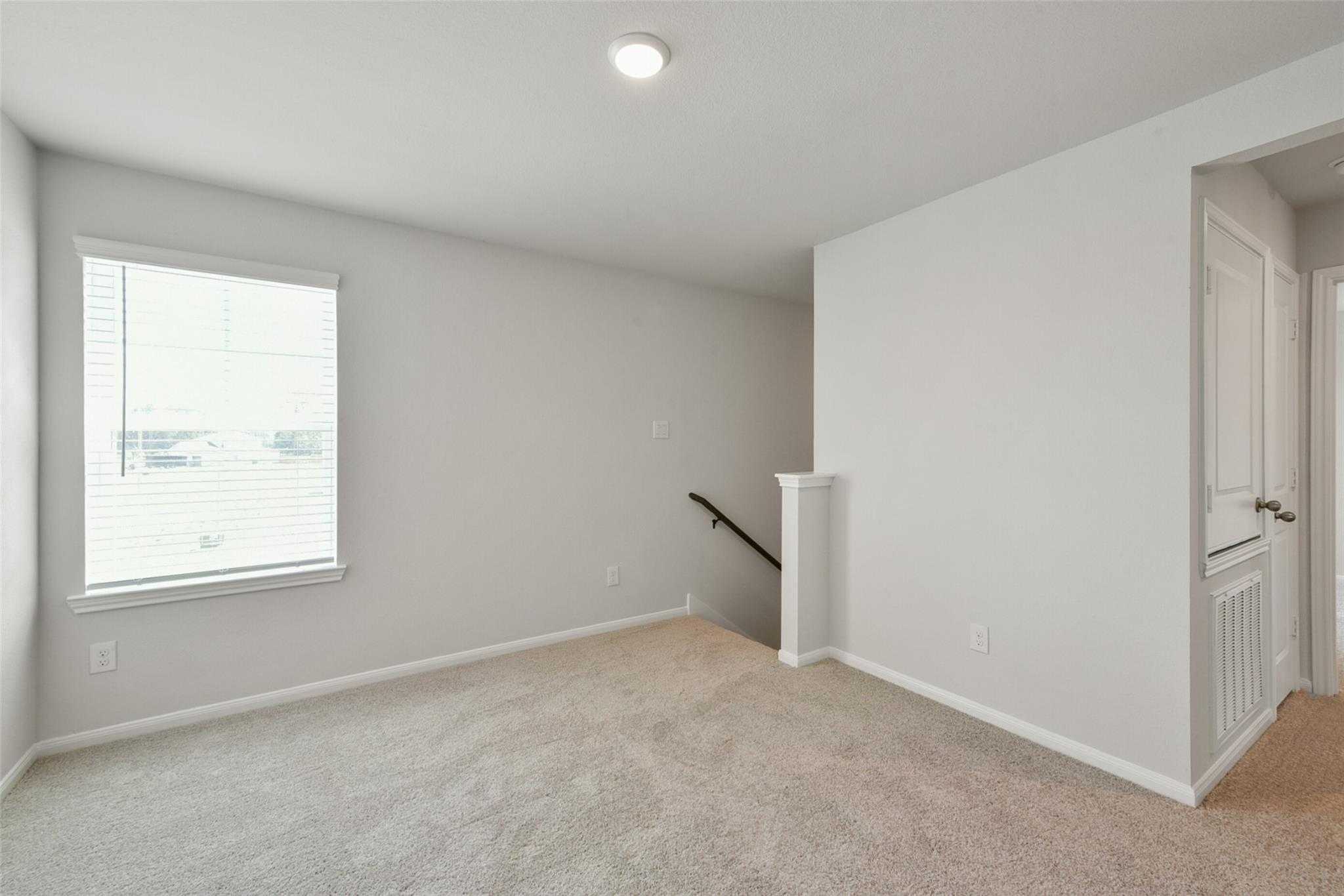 Bright upstairs loft with large window, beige carpet, and staircase in Davidson Homes The Sabine E, Dayton, Texas