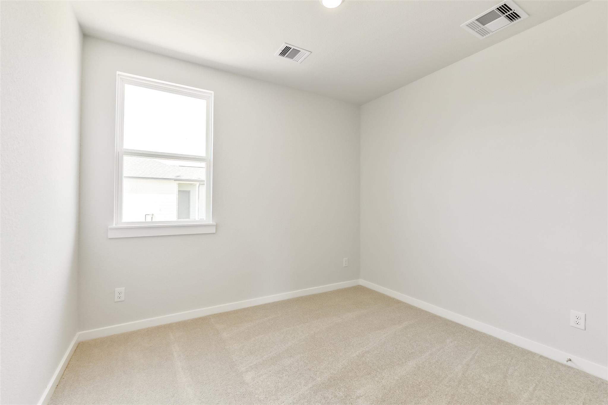 Bright empty secondary bedroom with light gray walls, beige carpet, and window in Davidson Homes The Frio G, Conroe TX