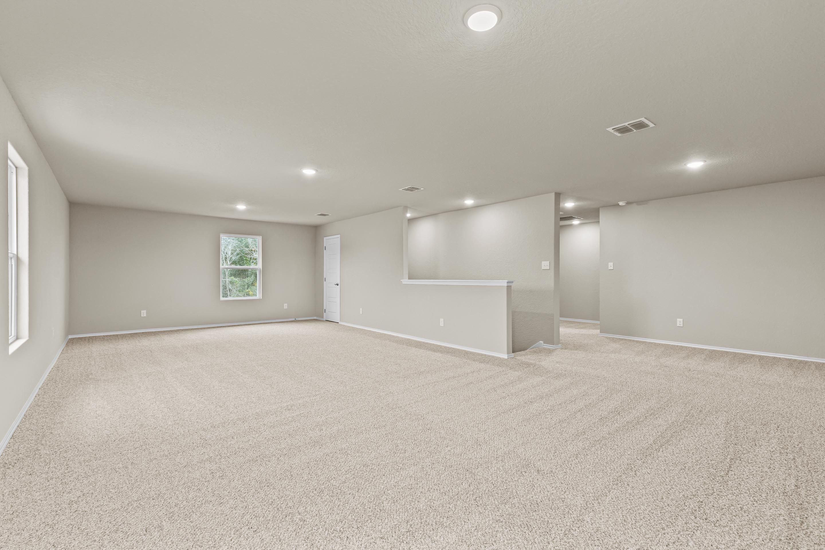Spacious upstairs loft with beige carpet, large windows, balcony railing, and recessed lighting in Davidson Homes The Douglas F, San Antonio