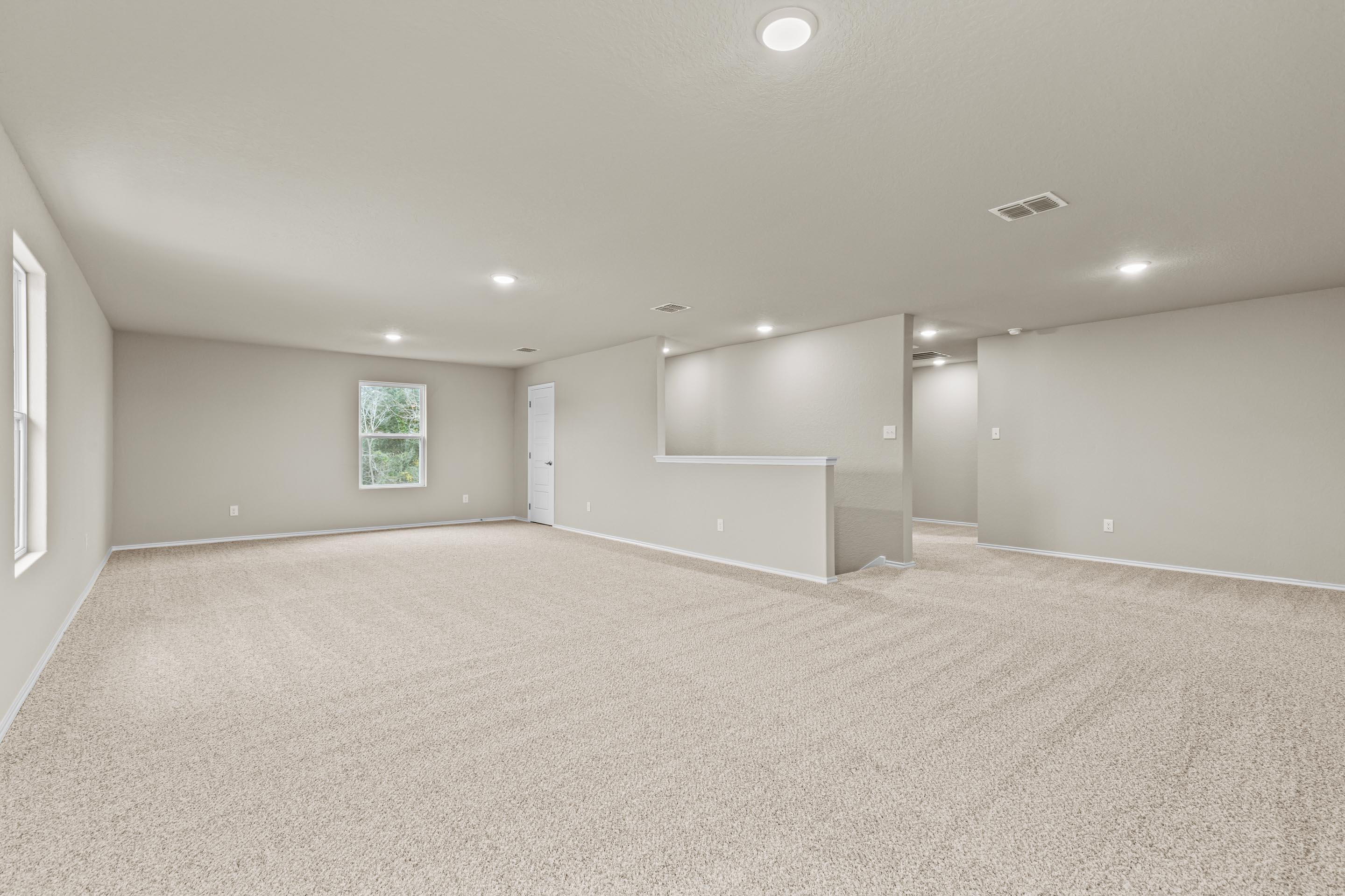 Spacious upstairs loft with beige carpet, large windows, balcony railing, and recessed lighting in Davidson Homes The Douglas F, San Antonio