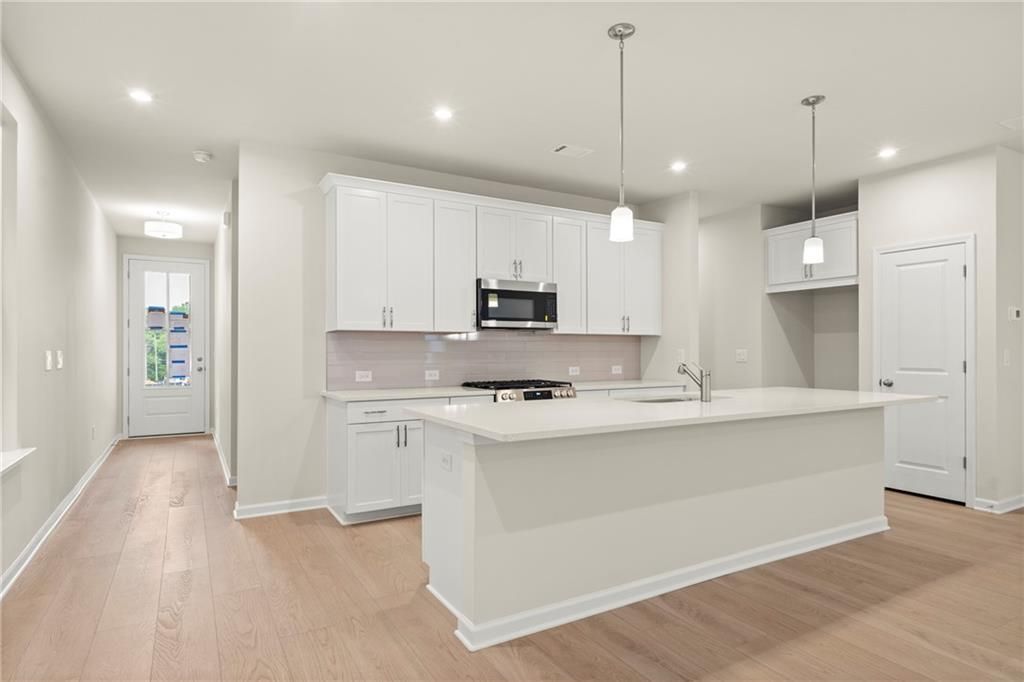 Modern white kitchen with large island, stainless steel appliances, and pendant lights in Davidson Homes The Cary A, Kennesaw, GA