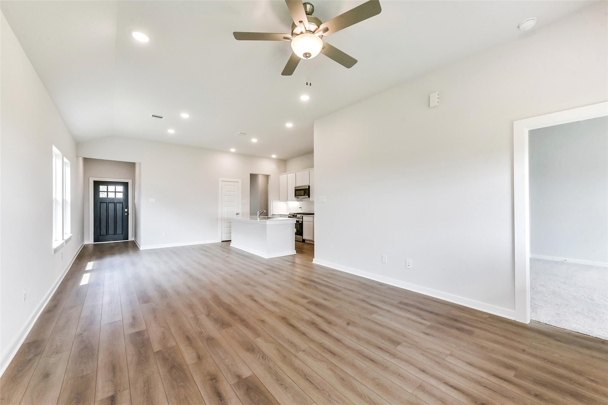 Open-concept living and kitchen with hardwood floors, white cabinets, island, and ceiling fan in Davidson Homes The Costa B, Dayton, Texas
