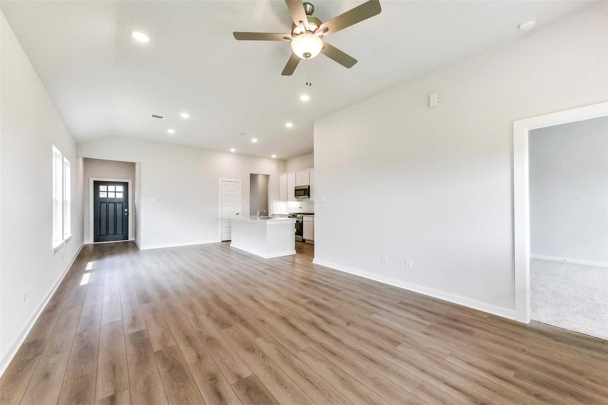 Open-concept living and kitchen with hardwood floors, white cabinets, island, and ceiling fan in Davidson Homes The Costa B, Dayton, Texas