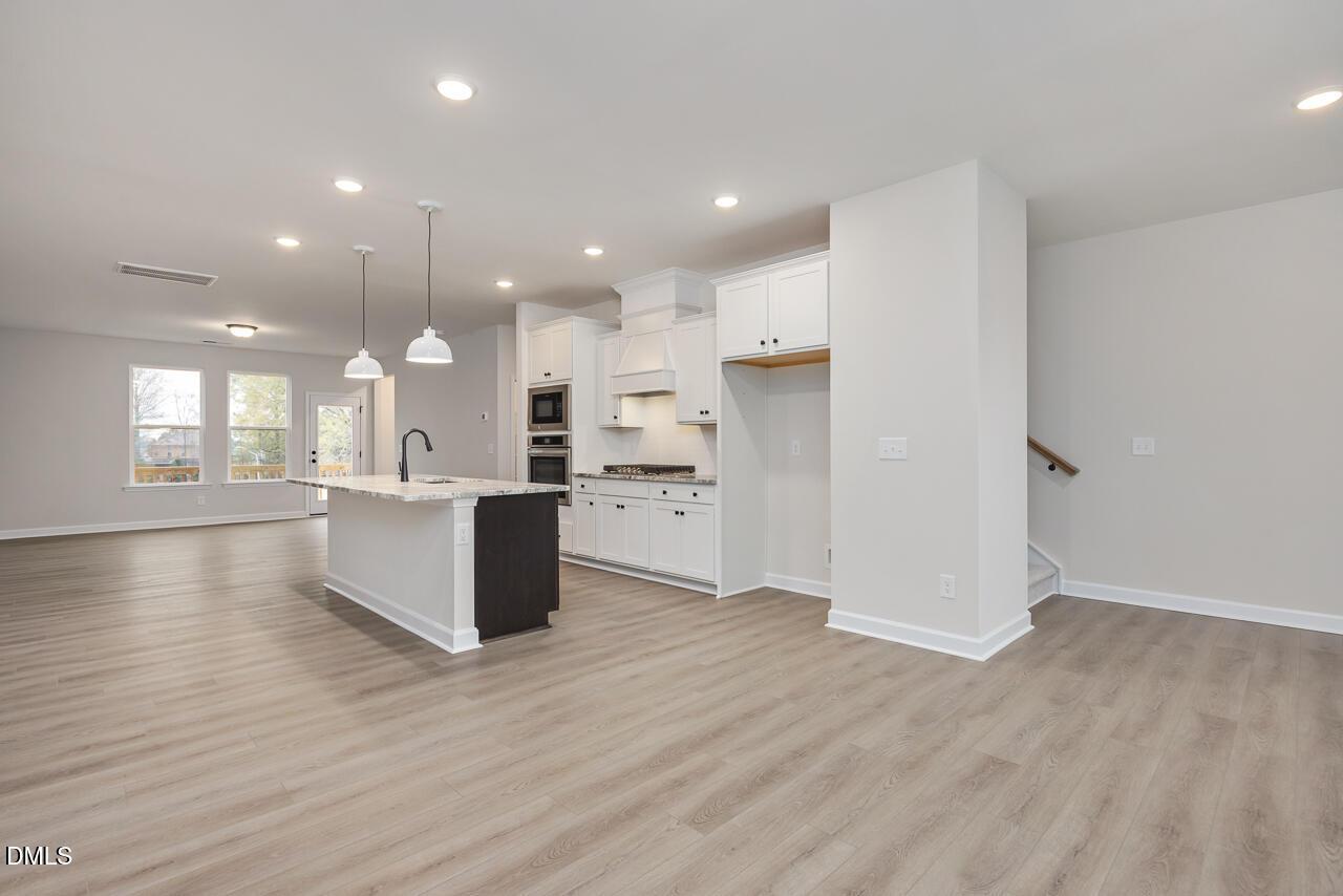 Modern white kitchen with quartz island, stainless double oven, pendant lights, and open floor plan in Davidson Homes The Mitchell, Knightdale, NC