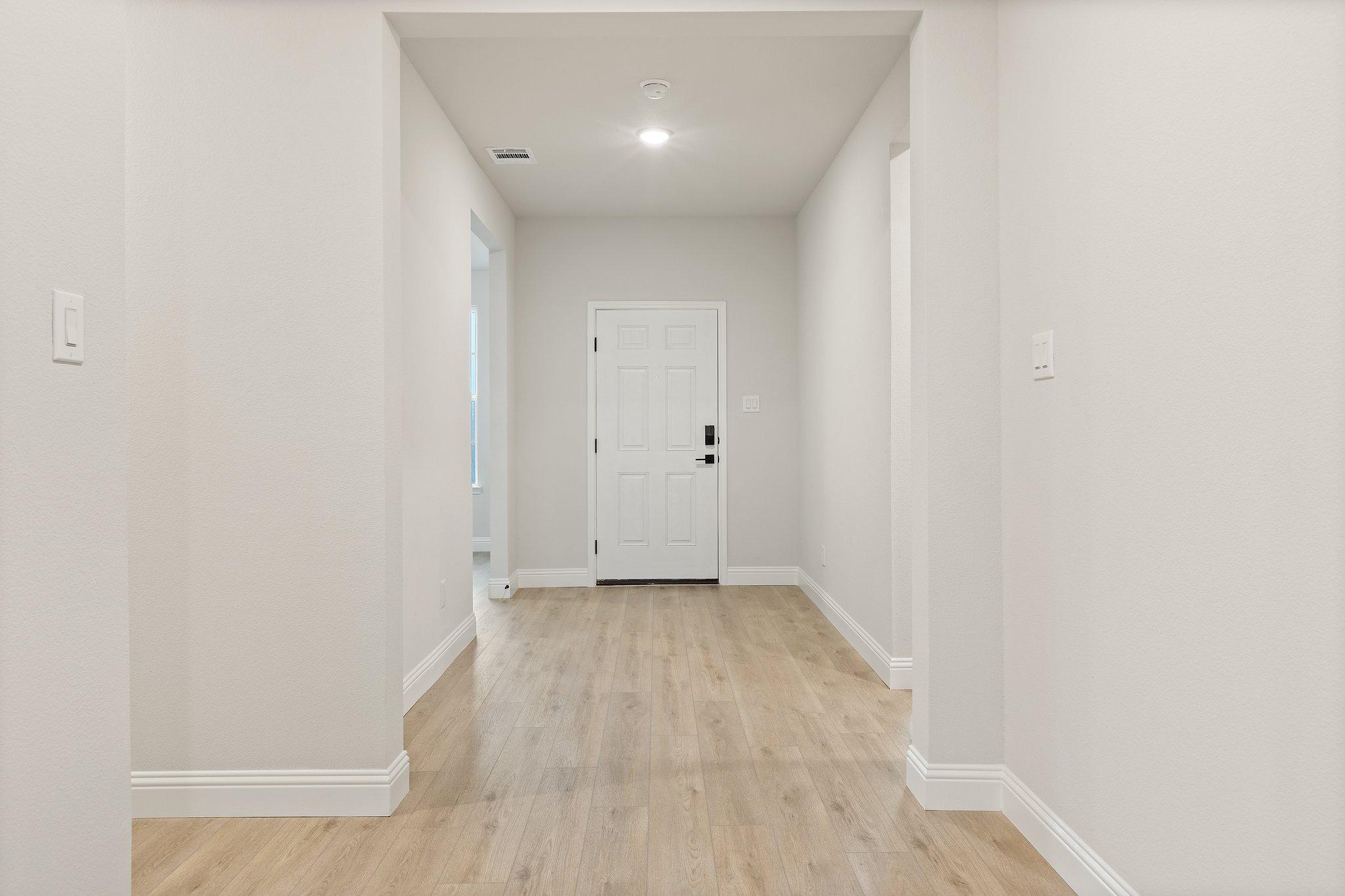 Spacious hallway in The Harrison D home with light oak floors, white walls, and entry door to master suite