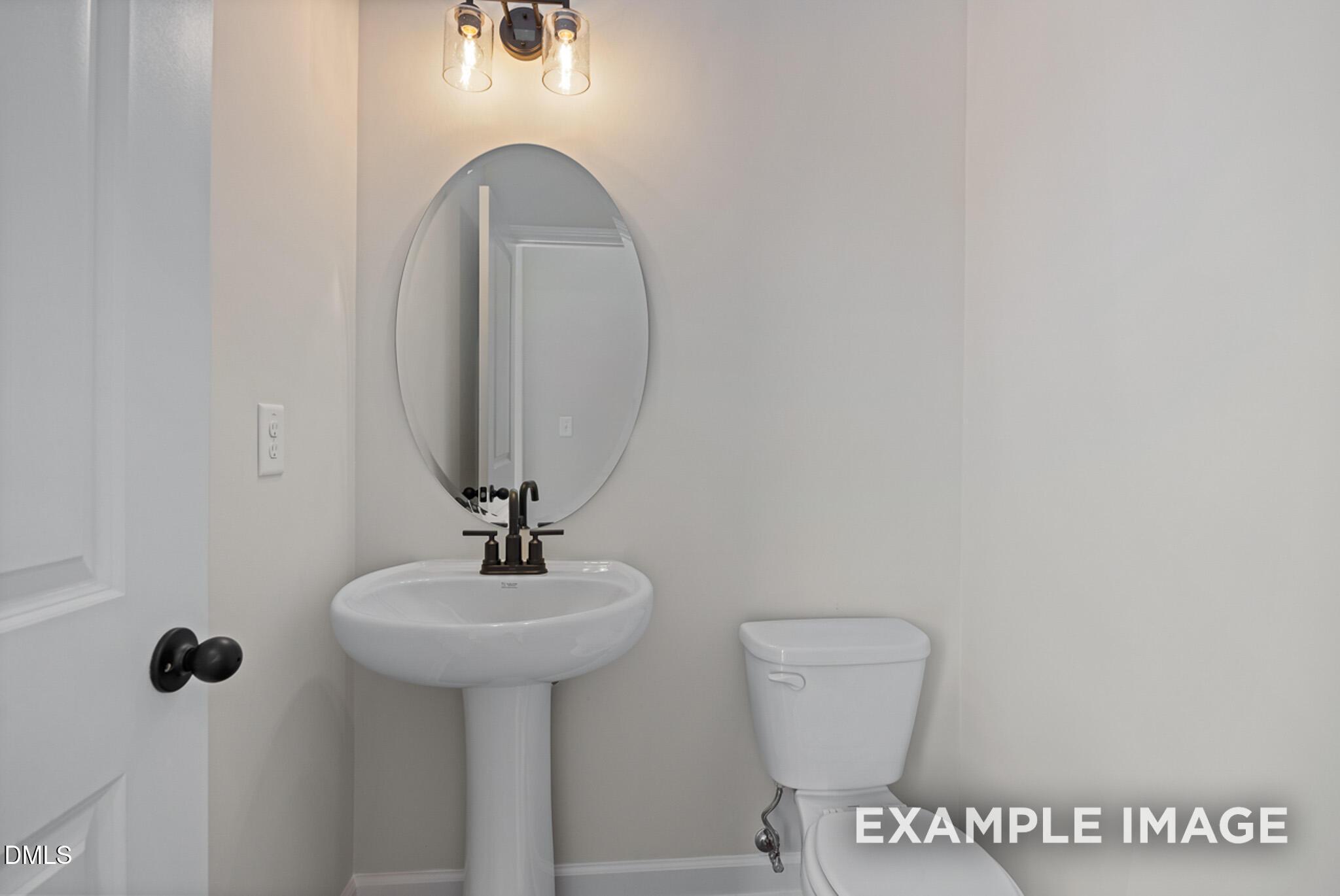 Modern powder room with pedestal sink, oval mirror, and lighting in The Mitchell floor plan at Camden Park, Knightdale, NC.