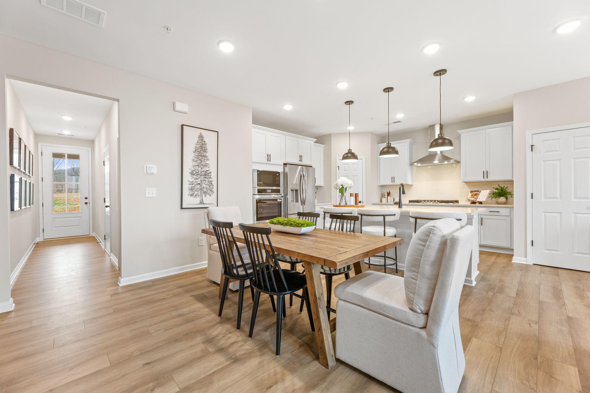 Open-concept kitchen and dining with white cabinets, stainless appliances, wooden table, and hardwood floors in The Durham B by Davidson Homes, Cumming, GA