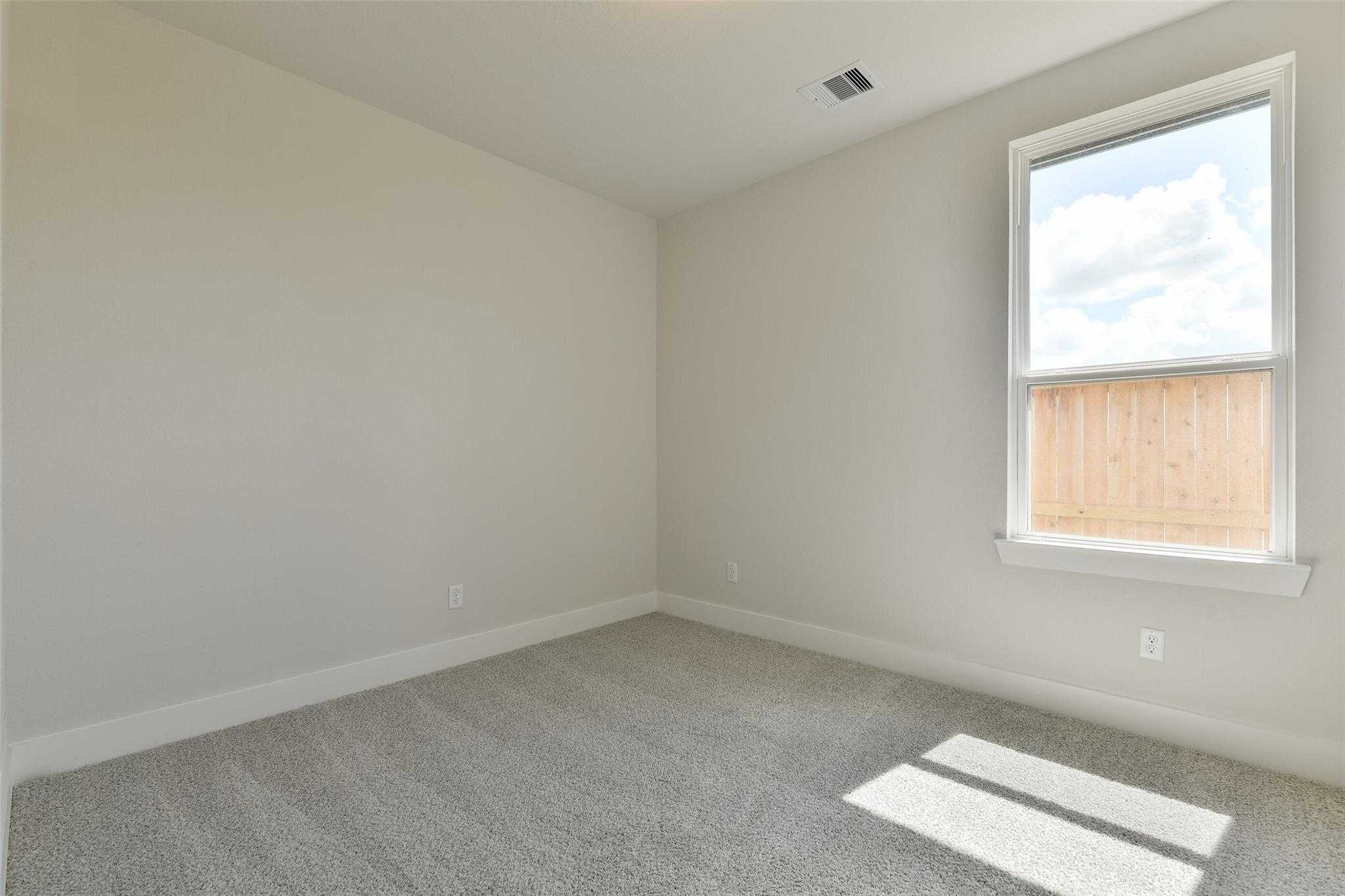 Bright secondary bedroom with beige walls, gray carpet, and window overlooking wooden fence in Davidson Homes The Edward A, Lago Mar, Texas