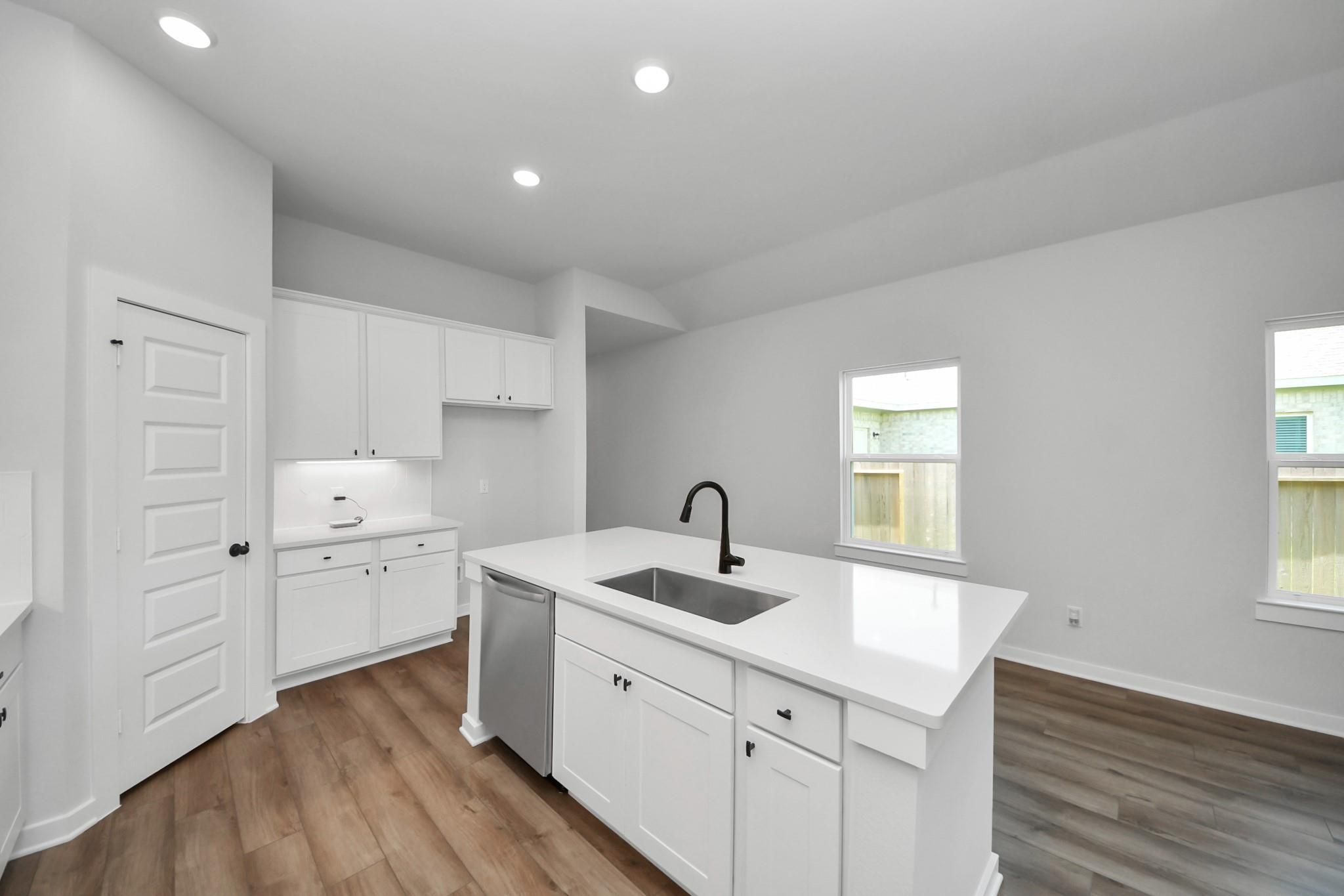 Modern kitchen with white cabinets, quartz island, and stainless steel appliances in The Riviera C floor plan, Dayton, TX.
