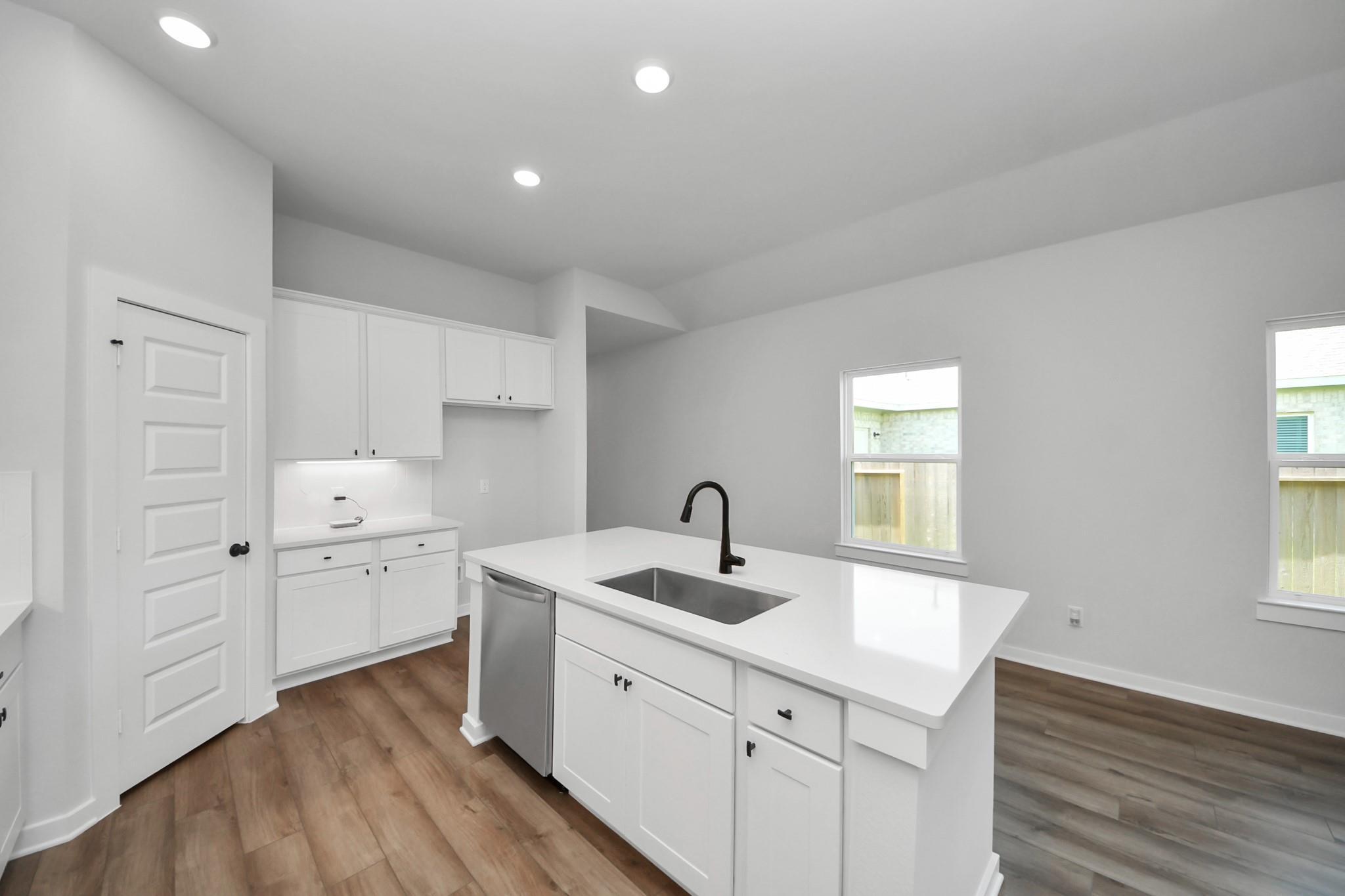 Modern kitchen with white cabinets, quartz island, and stainless steel appliances in The Riviera C floor plan, Dayton, TX.