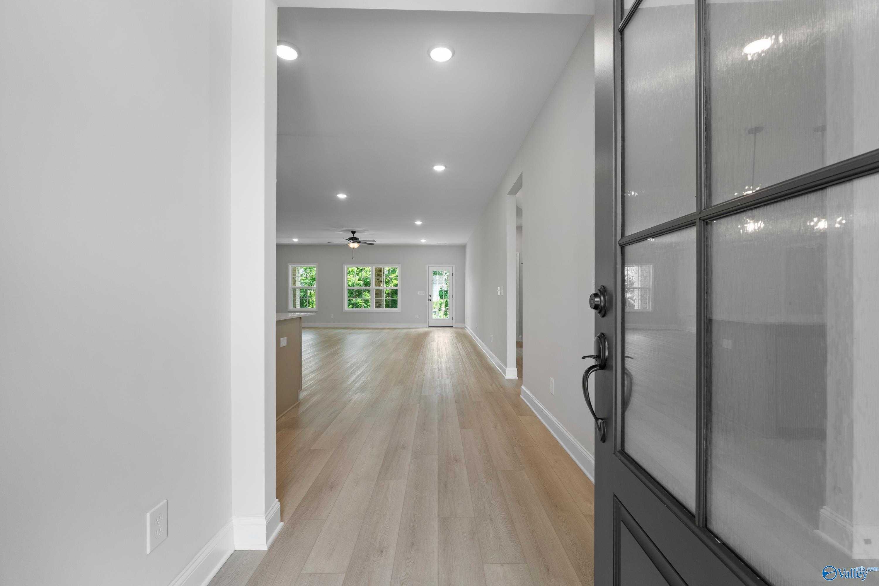 Bright open hallway leading to kitchen with island, hardwood floors, and large windows in Davidson Homes The Kirkland, Harvest AL