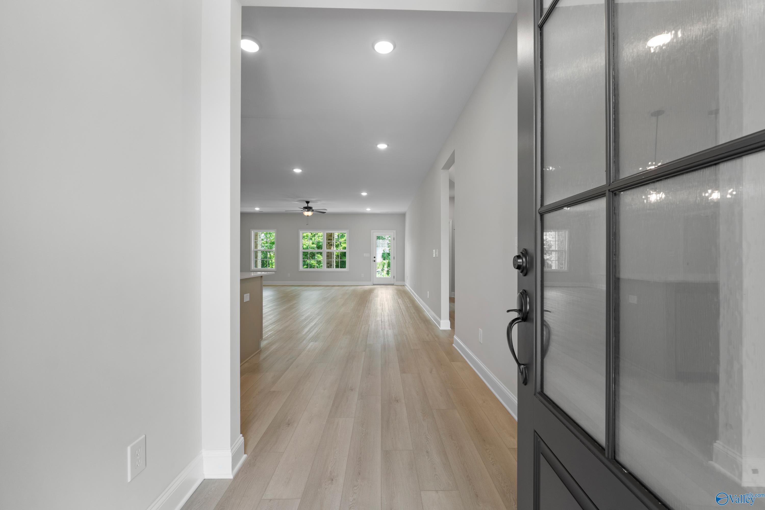Bright hallway with light oak floors, recessed lights, and glass door to open kitchen in Davidson Homes The Kirkland, Harvest AL