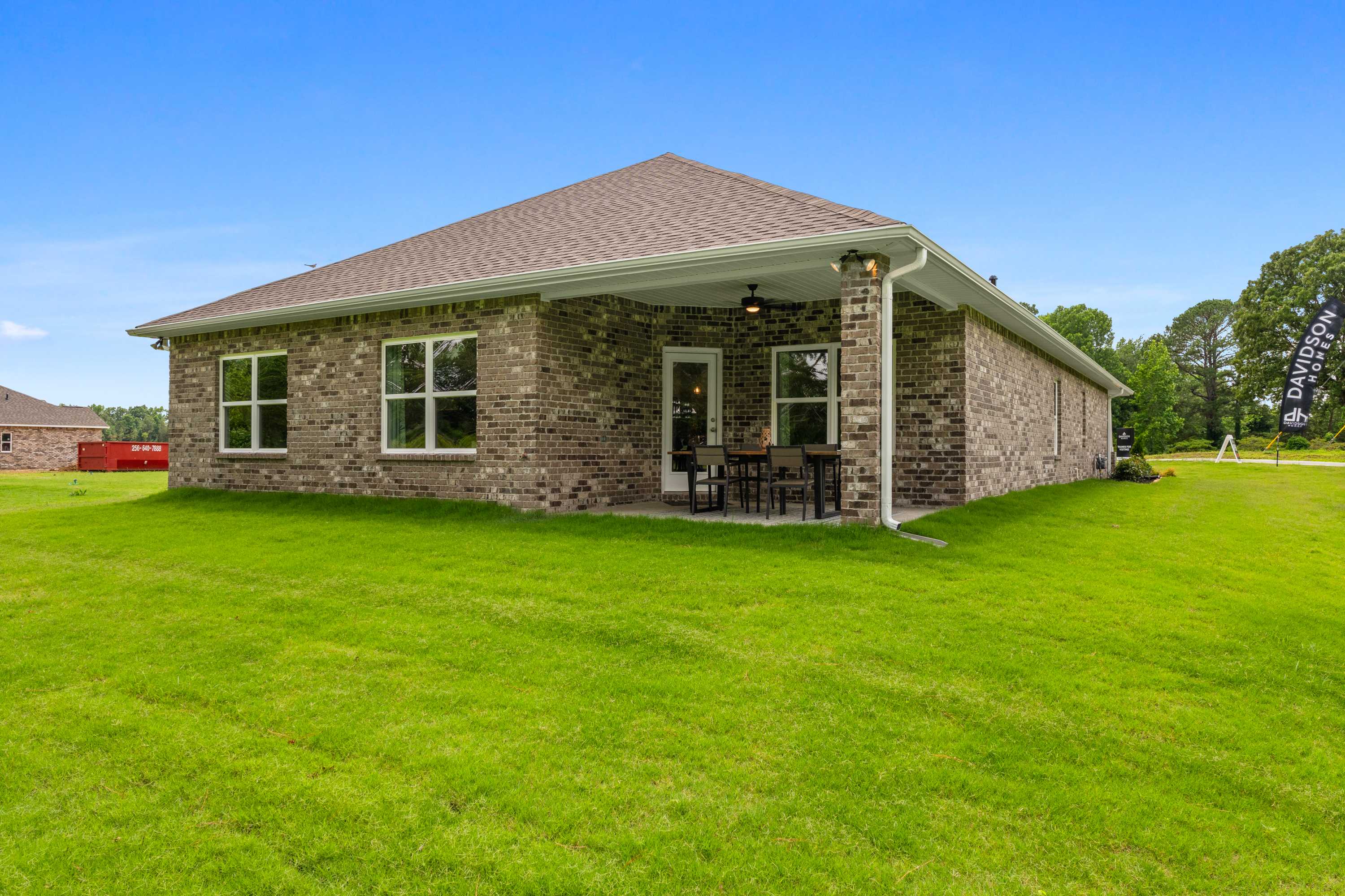 Brick home exterior at The Highlands in Arab, Alabama with covered patio, ceiling fan, seating, and lush green lawn