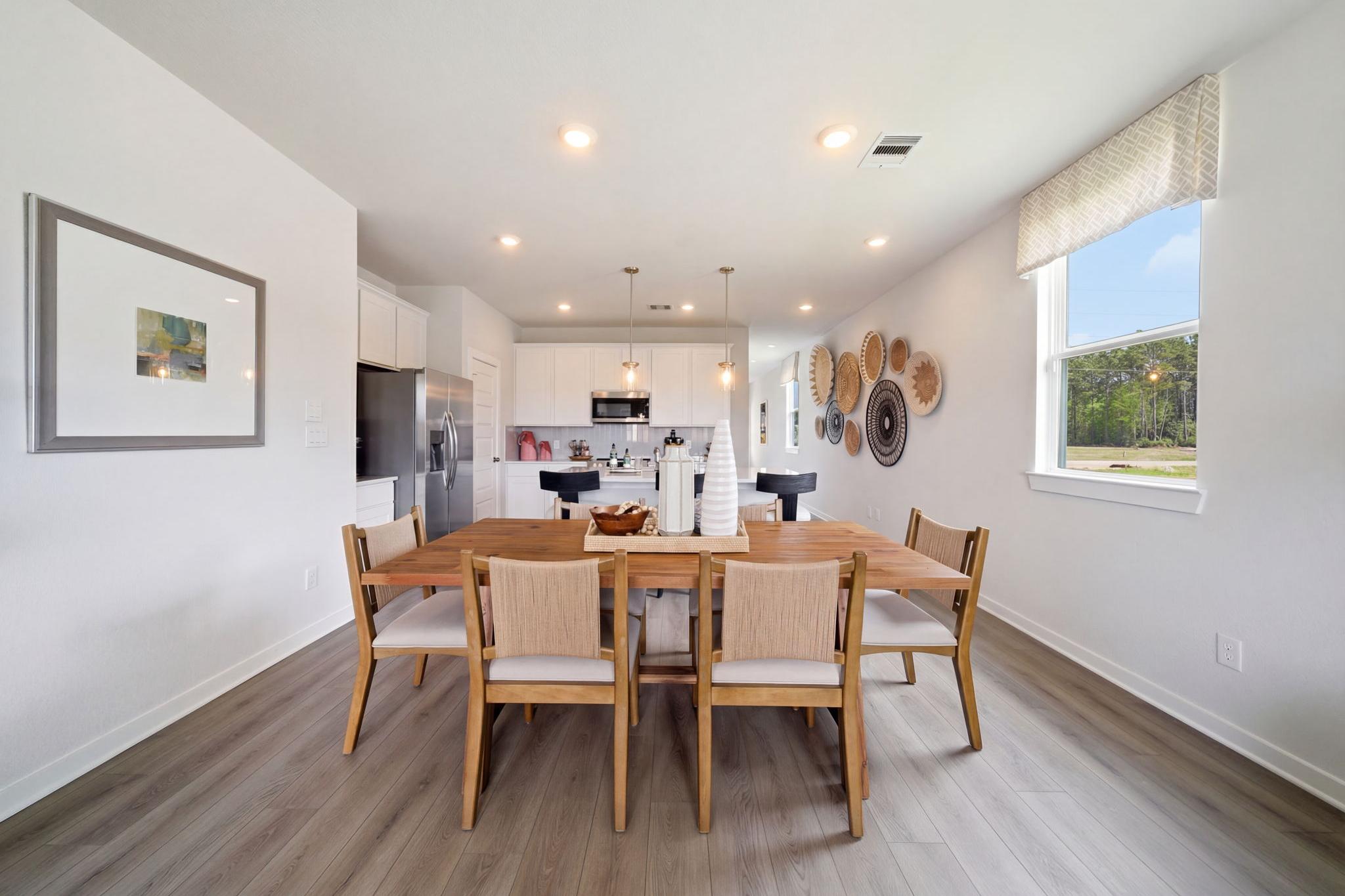 Open-concept dining area with wooden table and upholstered chairs adjacent to white kitchen at Spring Branch Crossing in Conroe Texas