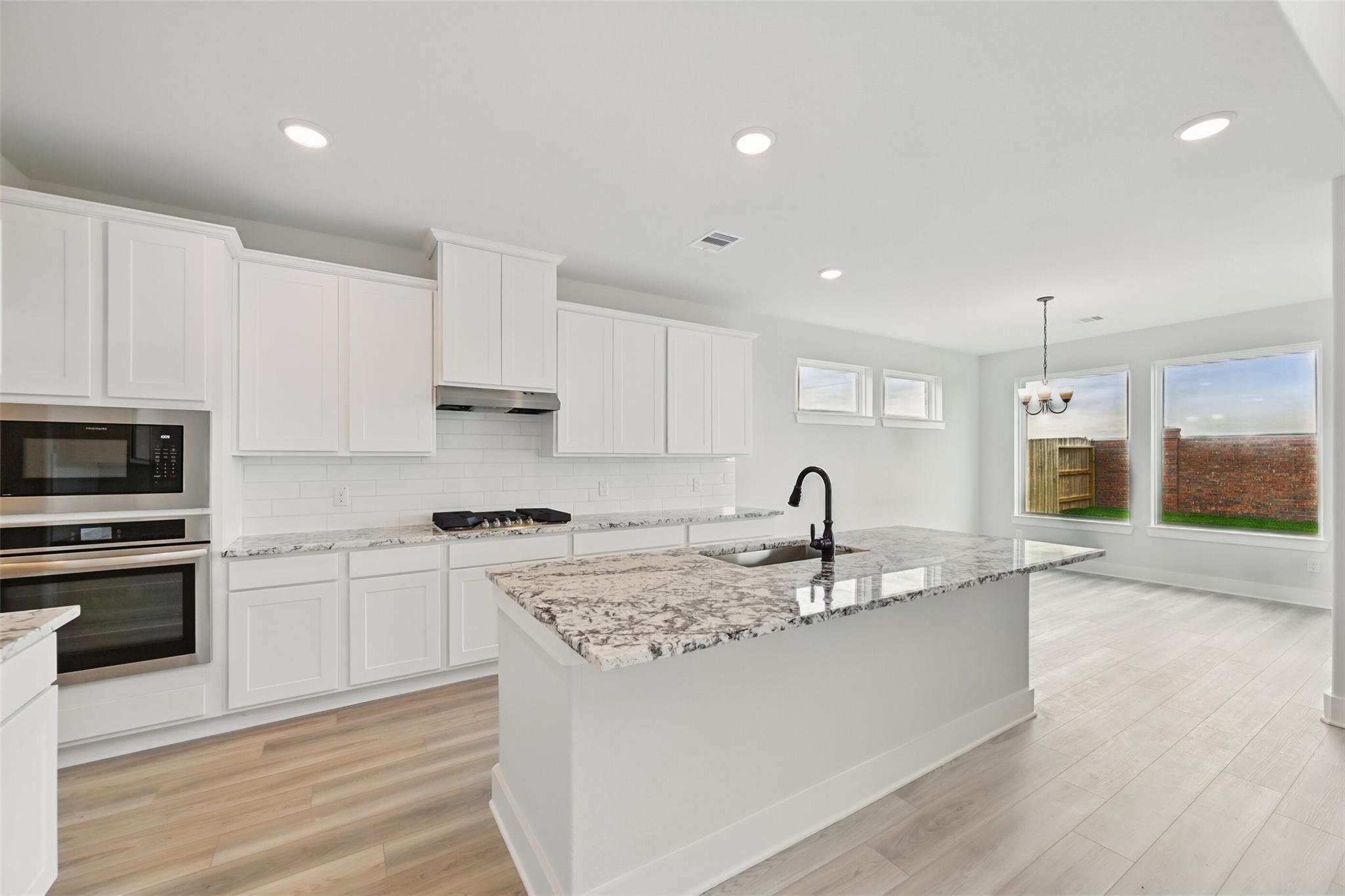 Modern white kitchen with granite island, stainless appliances, and open dining area in Davidson Homes The Victoria C, Lago Mar, Texas City