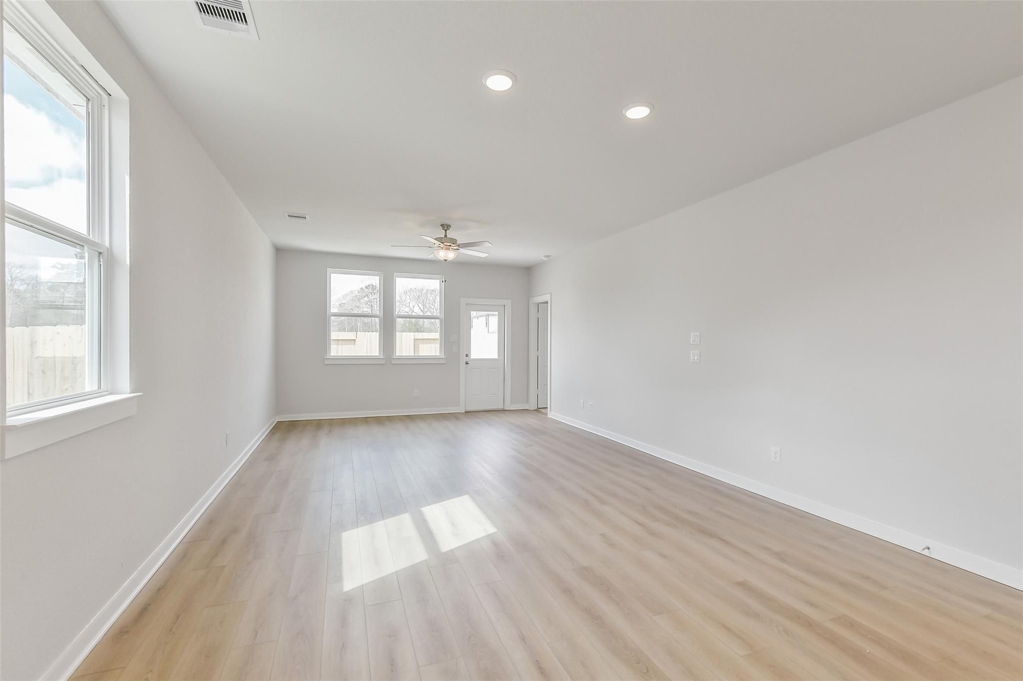 Bright living room with hardwood floors, large windows, and ceiling fan in 3-bedroom Davidson Homes The Frio G, Cleveland, Texas