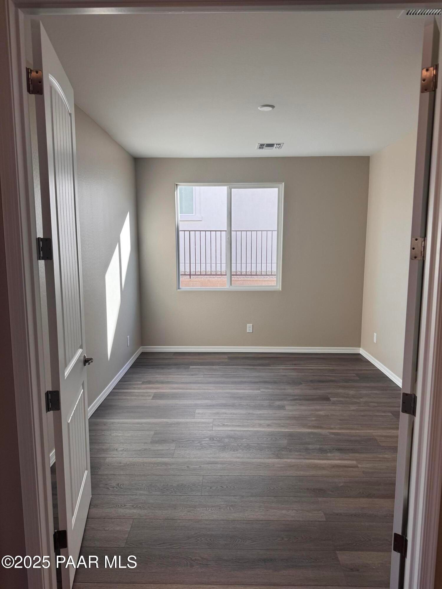 Empty bedroom featuring beige walls, gray hardwood floors, and balcony window in Davidson Homes The Sunrise II A, Prescott, AZ