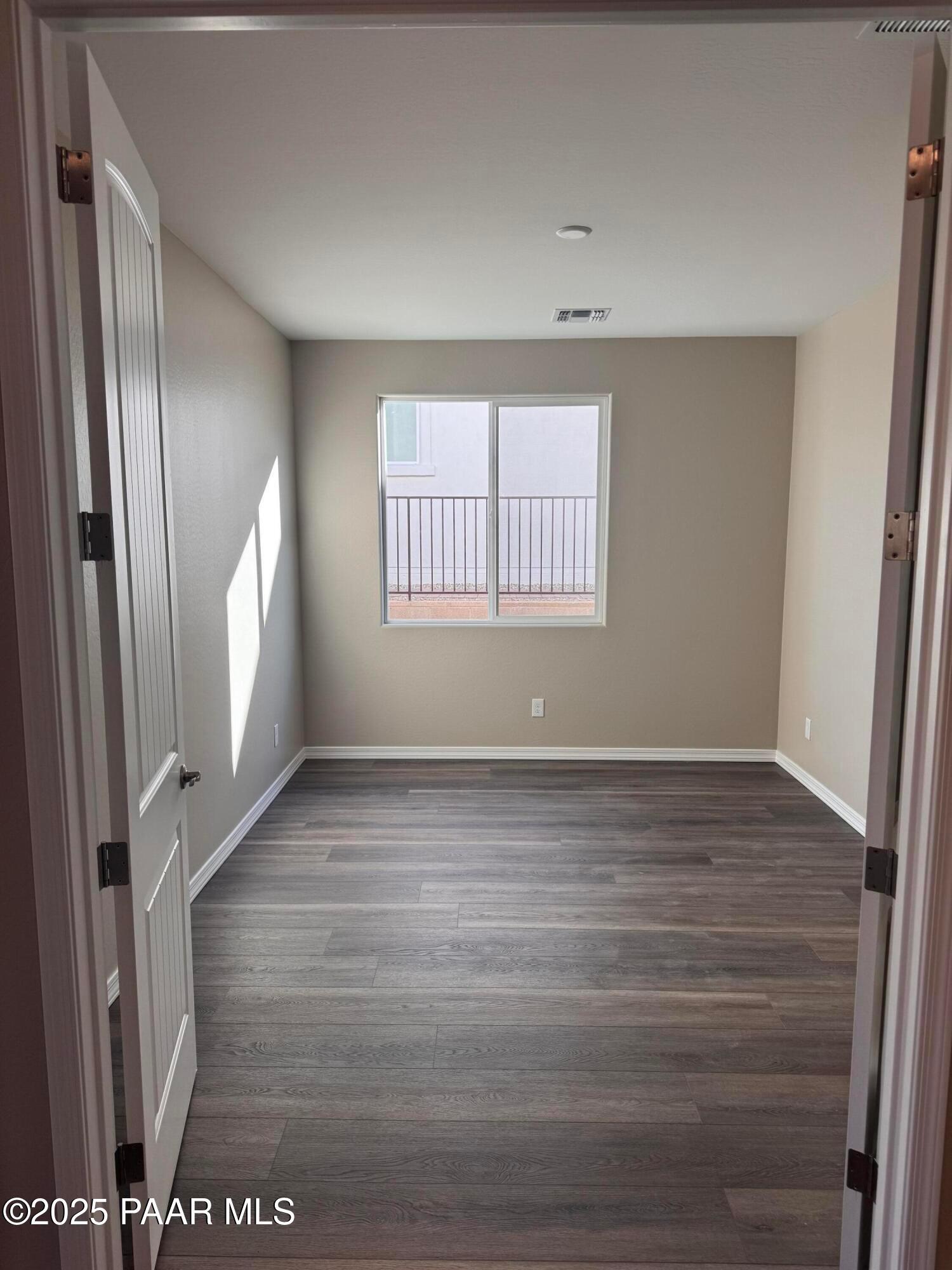 Empty bedroom featuring beige walls, gray hardwood floors, and balcony window in Davidson Homes The Sunrise II A, Prescott, AZ