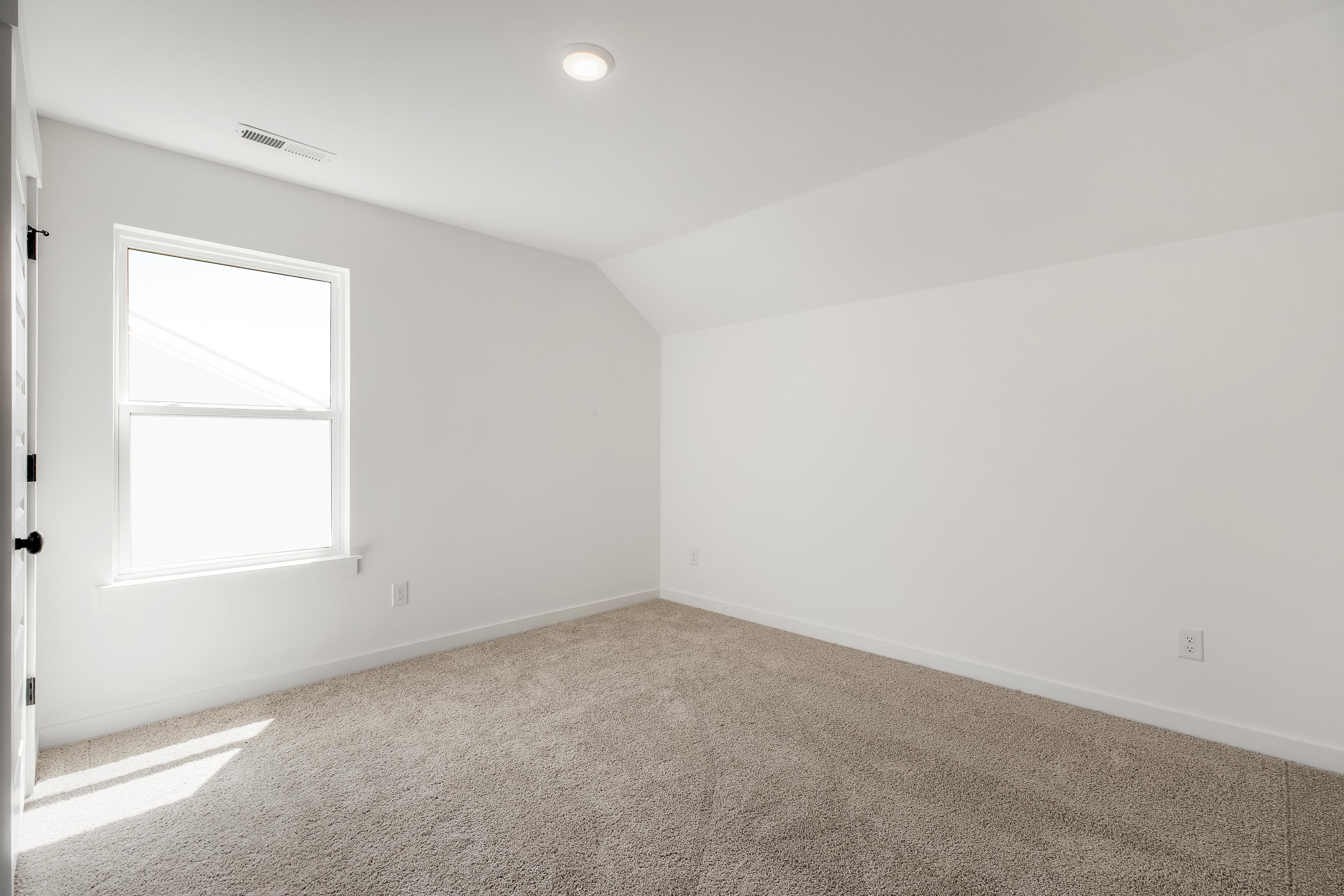 Bright, neutral bedroom in The Cedar D floor plan by Davidson Homes featuring plush carpeting and natural light.