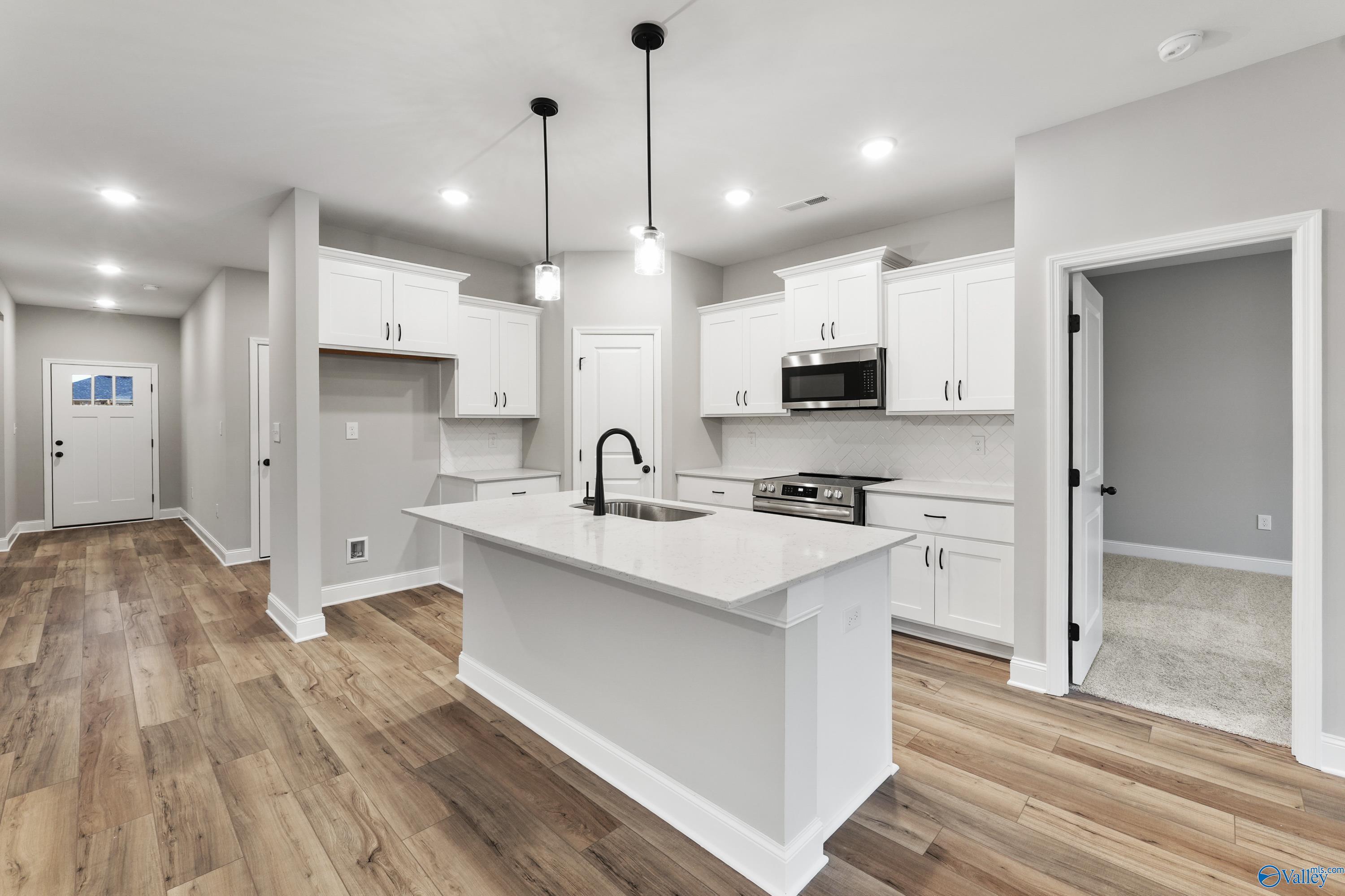Modern white kitchen with quartz island, stainless appliances, pendant lights, and hardwood floors in Davidson Homes Asheville C, Meridianville AL