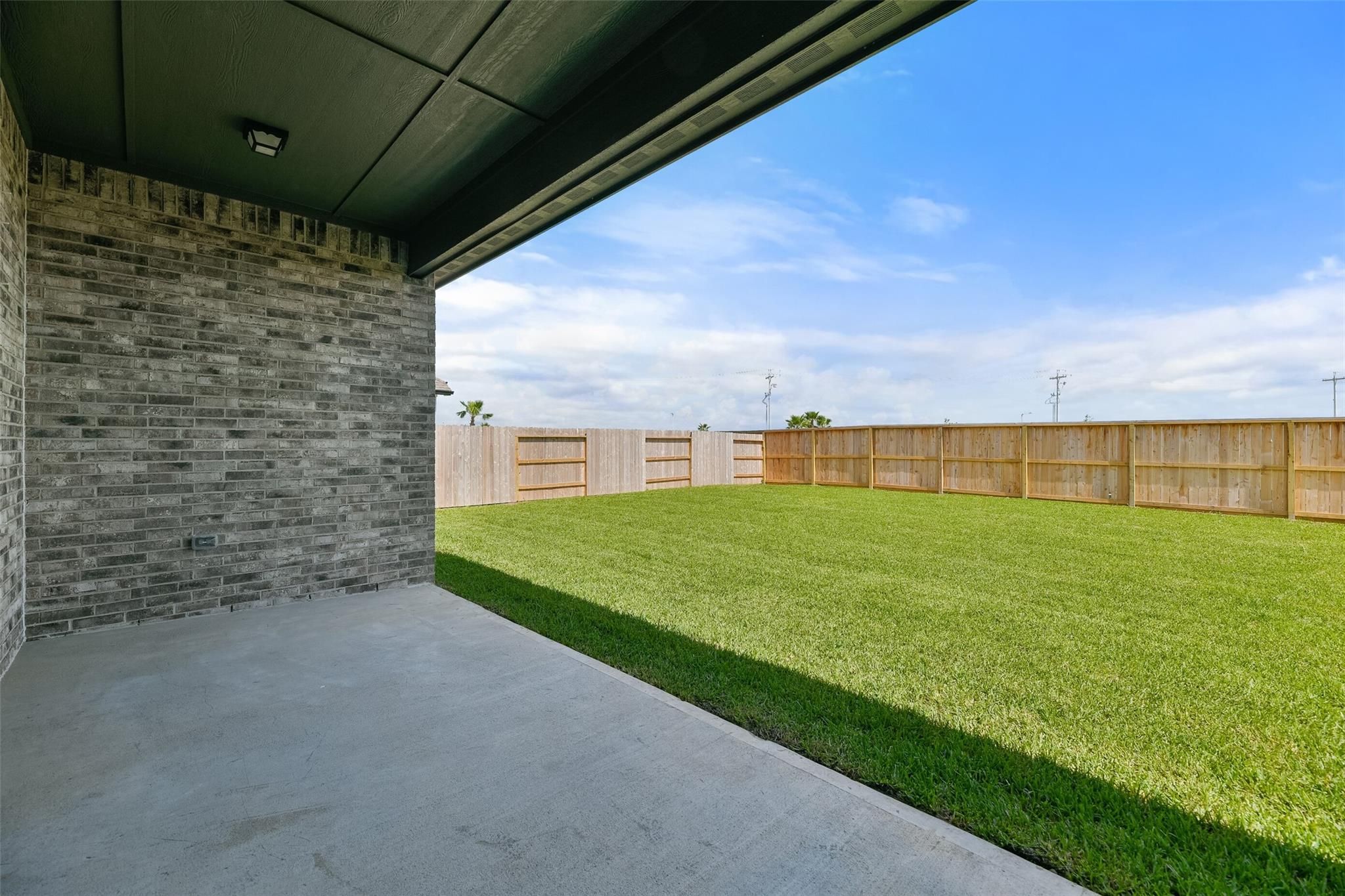 Covered back patio with brick walls overlooking lush green backyard and wooden fence in Davidson Homes Edward A, Lago Mar Texas